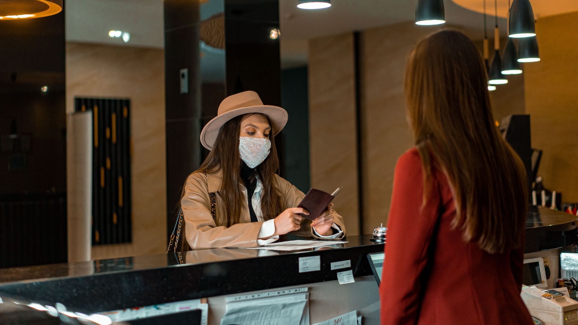 A woman wearing a mask checks in at a hotel reception desk.
