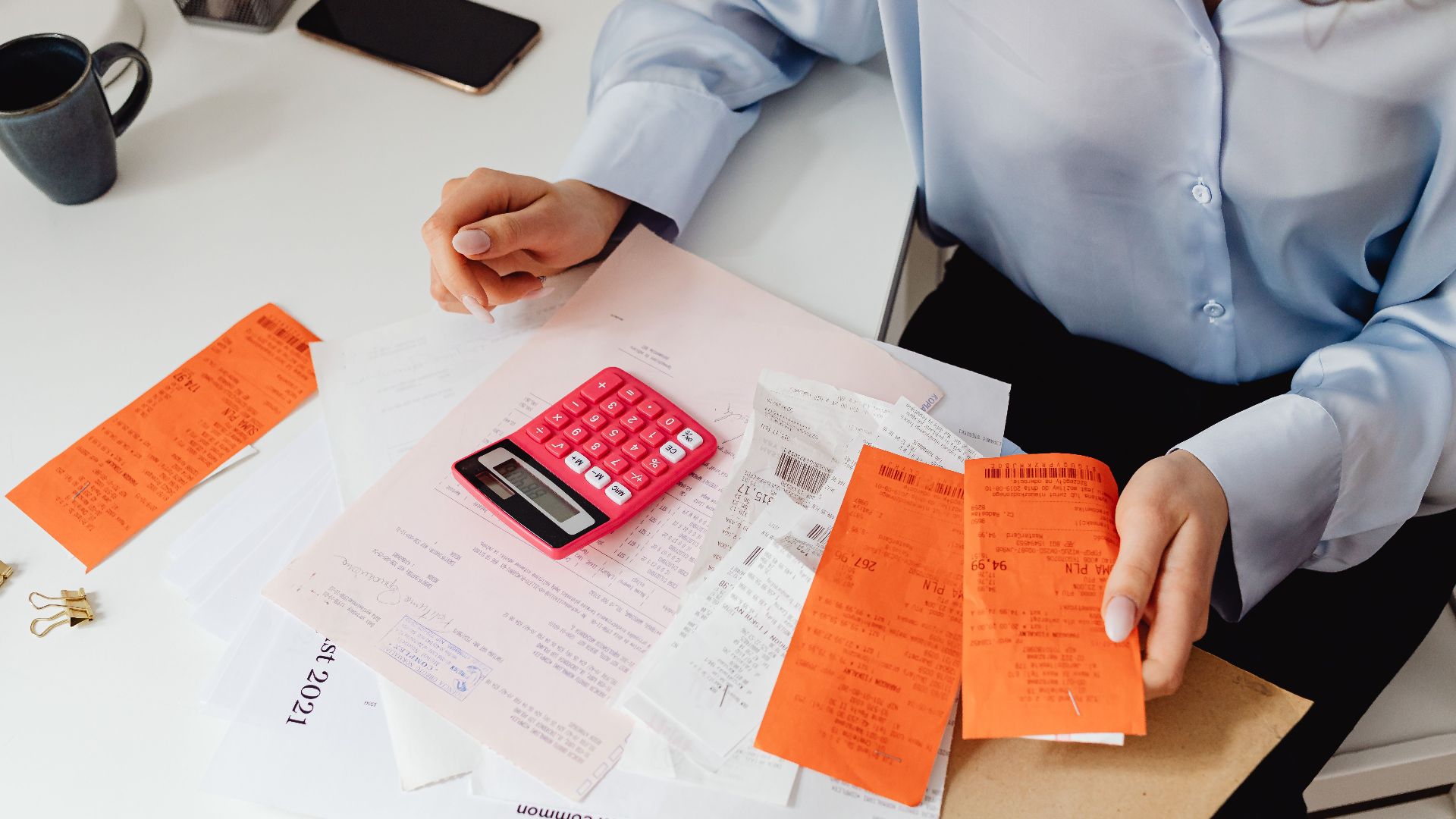 A woman reviews receipts and calculates expenses at a desk with a pink calculator.
