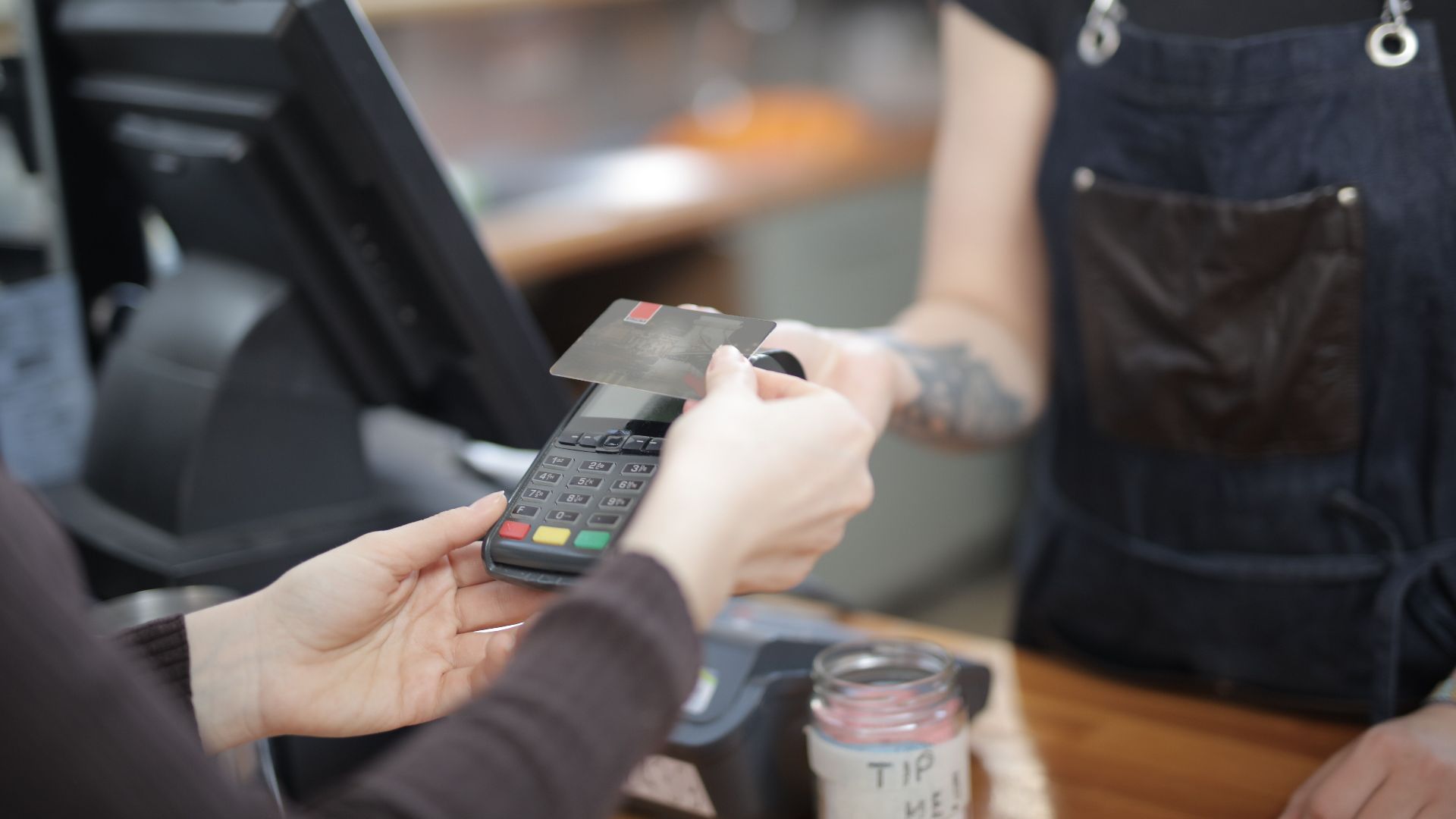 Close-up of customer and cashier during a credit card transaction at a store counter indoors.