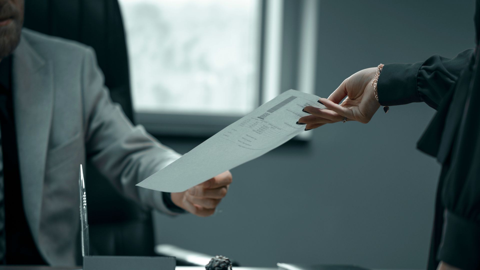 A formal business interaction with document exchange between professionals in a modern office setting.