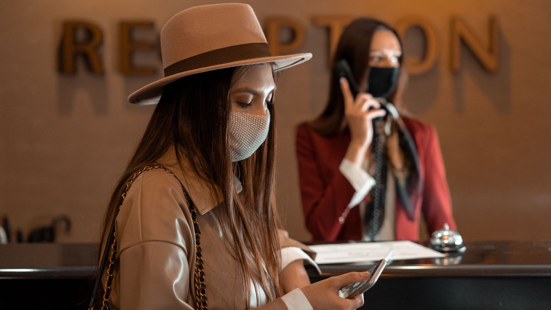 Woman wearing a mask checking her phone at a hotel reception during COVID-19.
