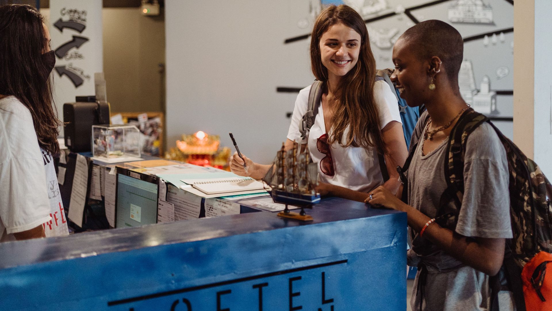 Three travelers checking into a hostel at the reception desk, showcasing hospitality and adventure.