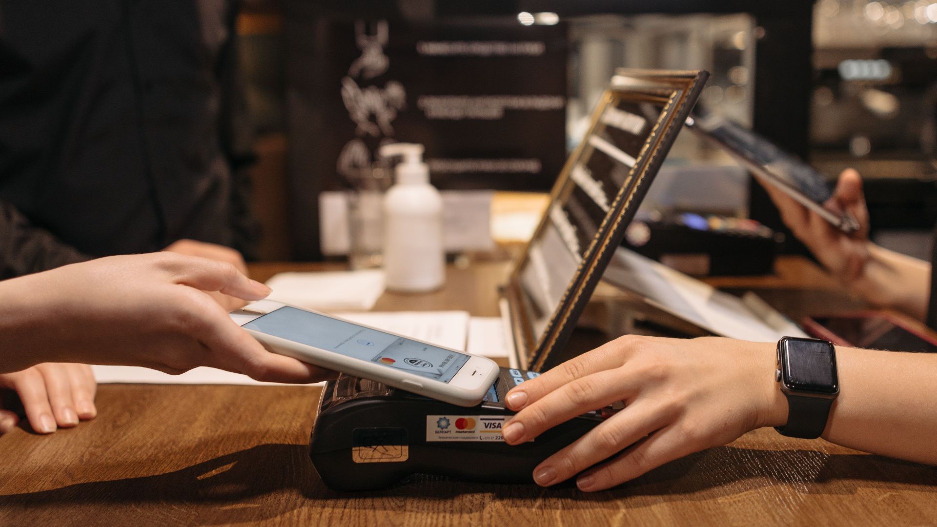 Hands using mobile for contactless payment at café terminal.