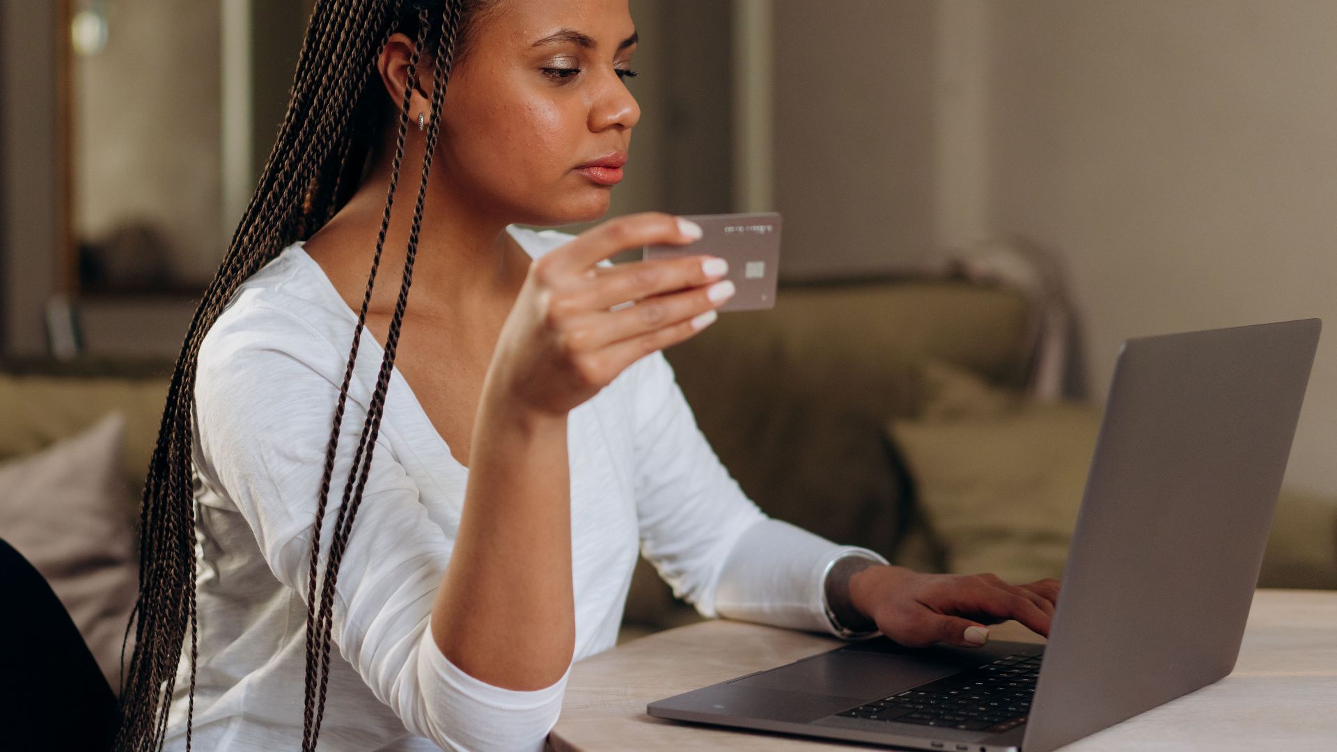 A woman with braided hair makes an online transaction using a credit card and laptop at home.