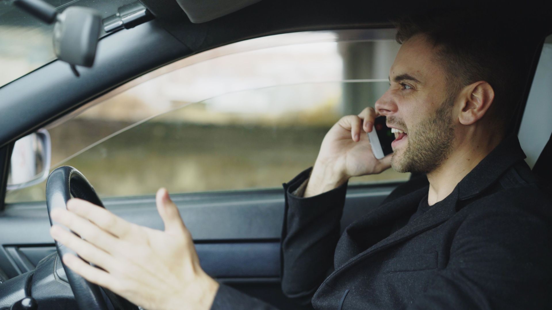Man in car talking on cell phone while driving, displaying frustration