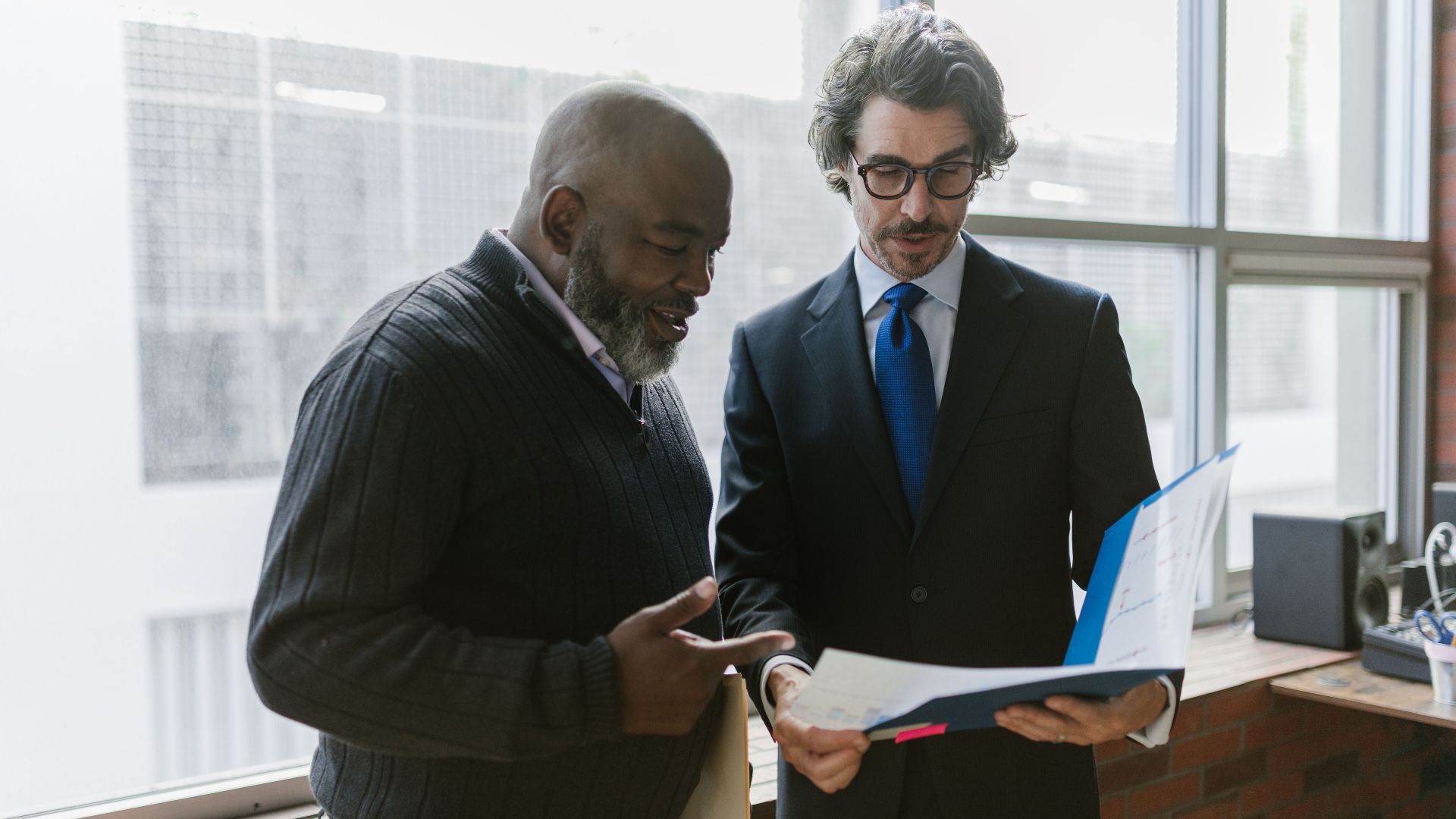 Two businessmen discussing and reviewing documents in a modern office setting.
