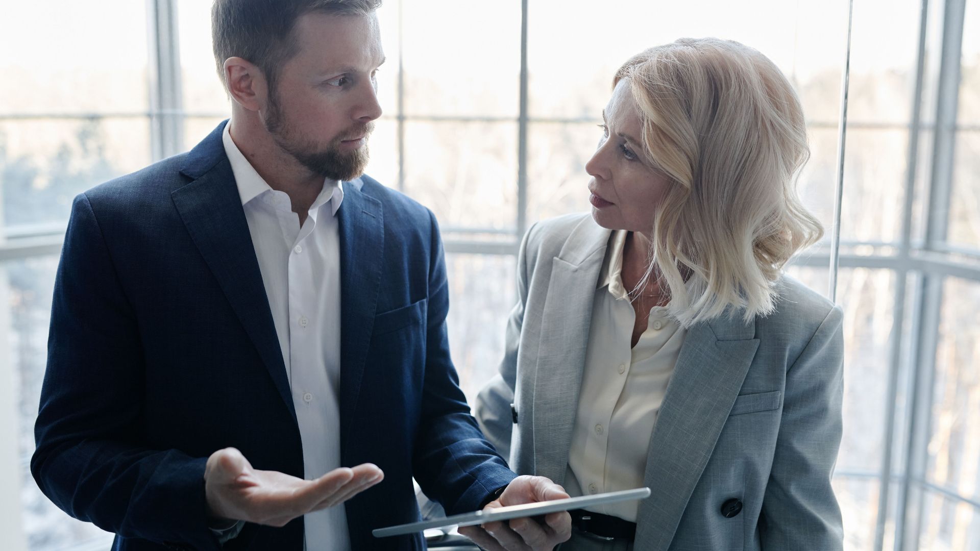 Two business professionals engaged in a discussion with a tablet in a corporate setting.
