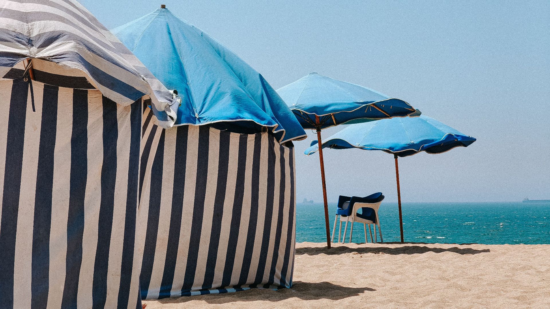 Striped tents and blue umbrellas on the sandy beach of Figueira da Foz, Portugal, with a serene ocean view.