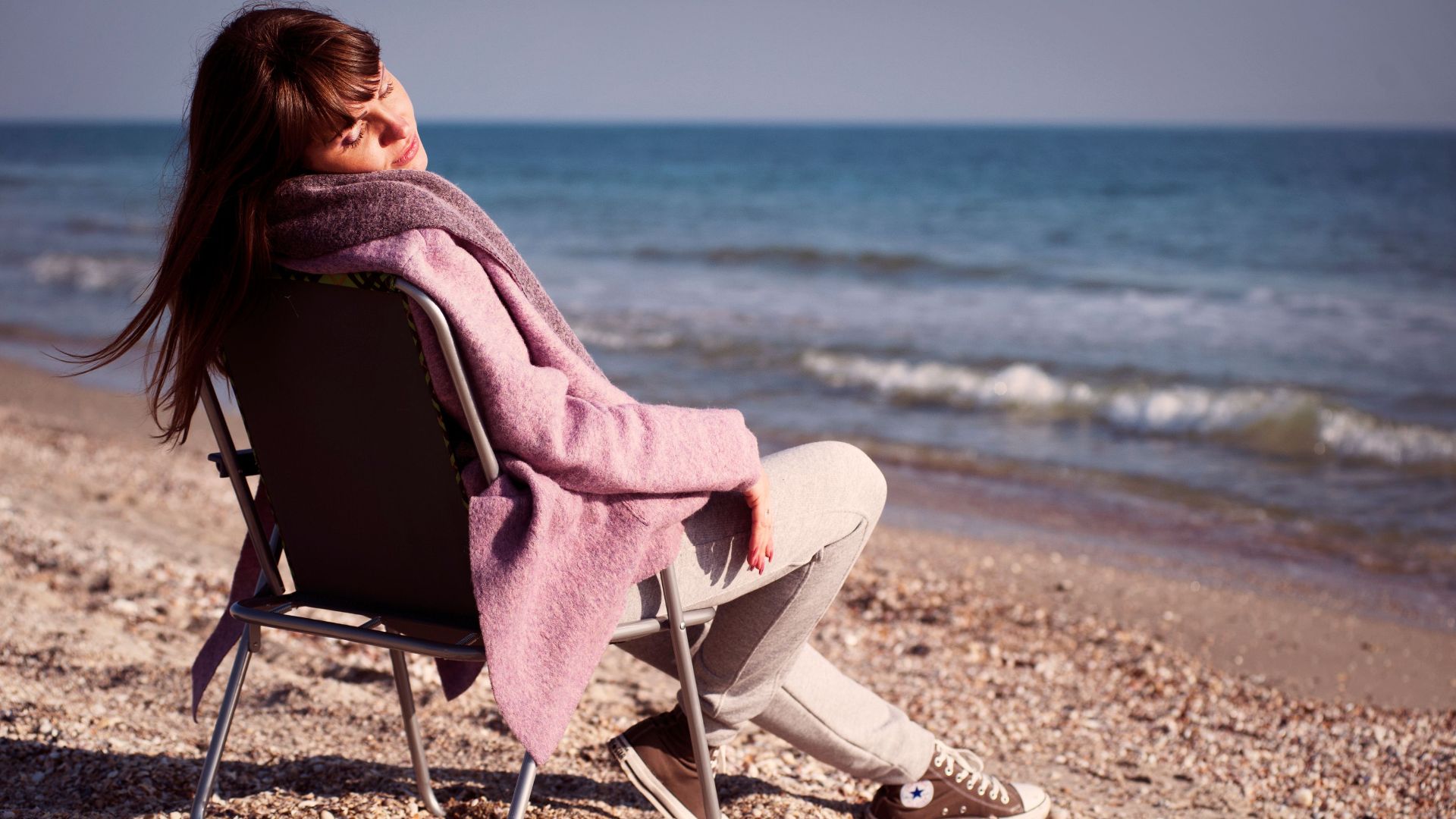 A woman in casual attire enjoying a relaxing day by the ocean on a sunny beach.