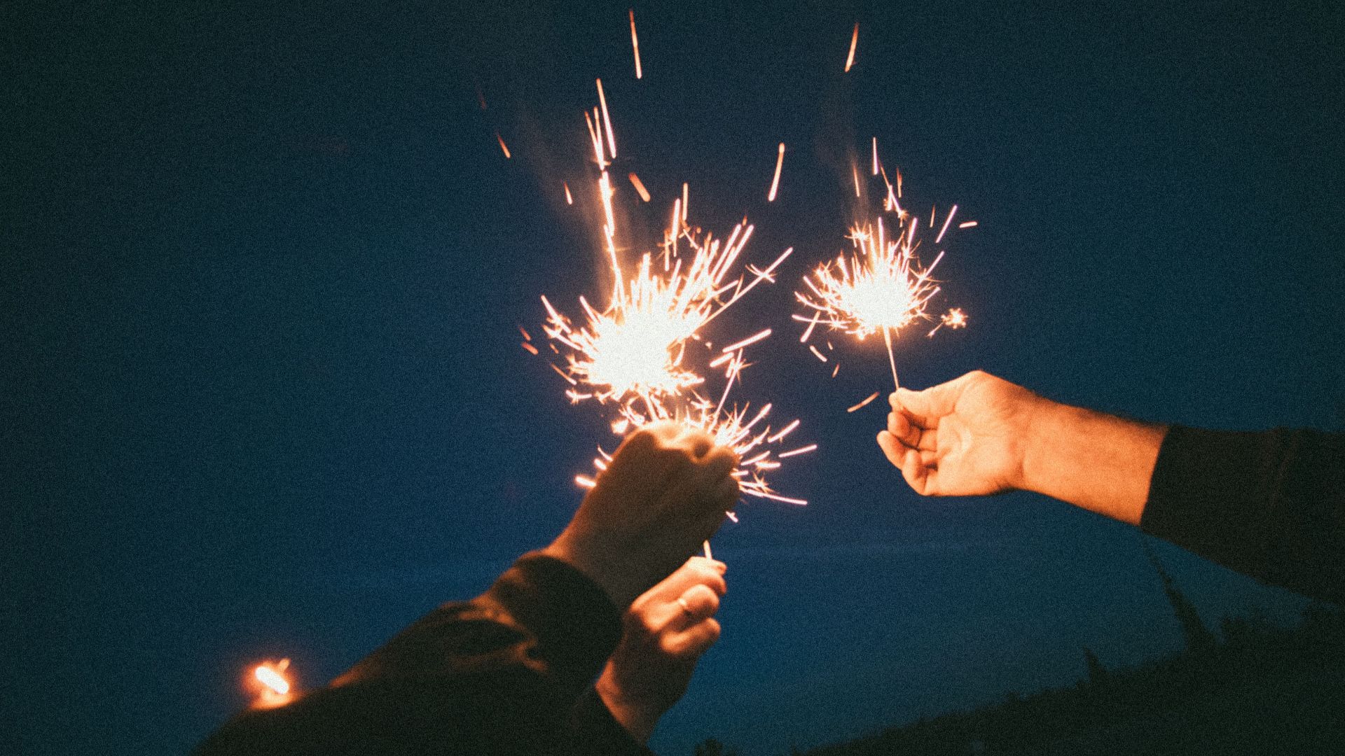 Hands holding sparklers illuminate the night, creating a festive atmosphere during an outdoor celebration.