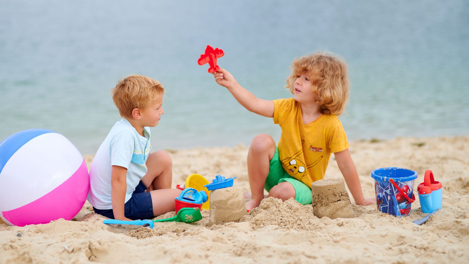 Two kids enjoy playing with toys on a sunny beach day, building sandcastles together.