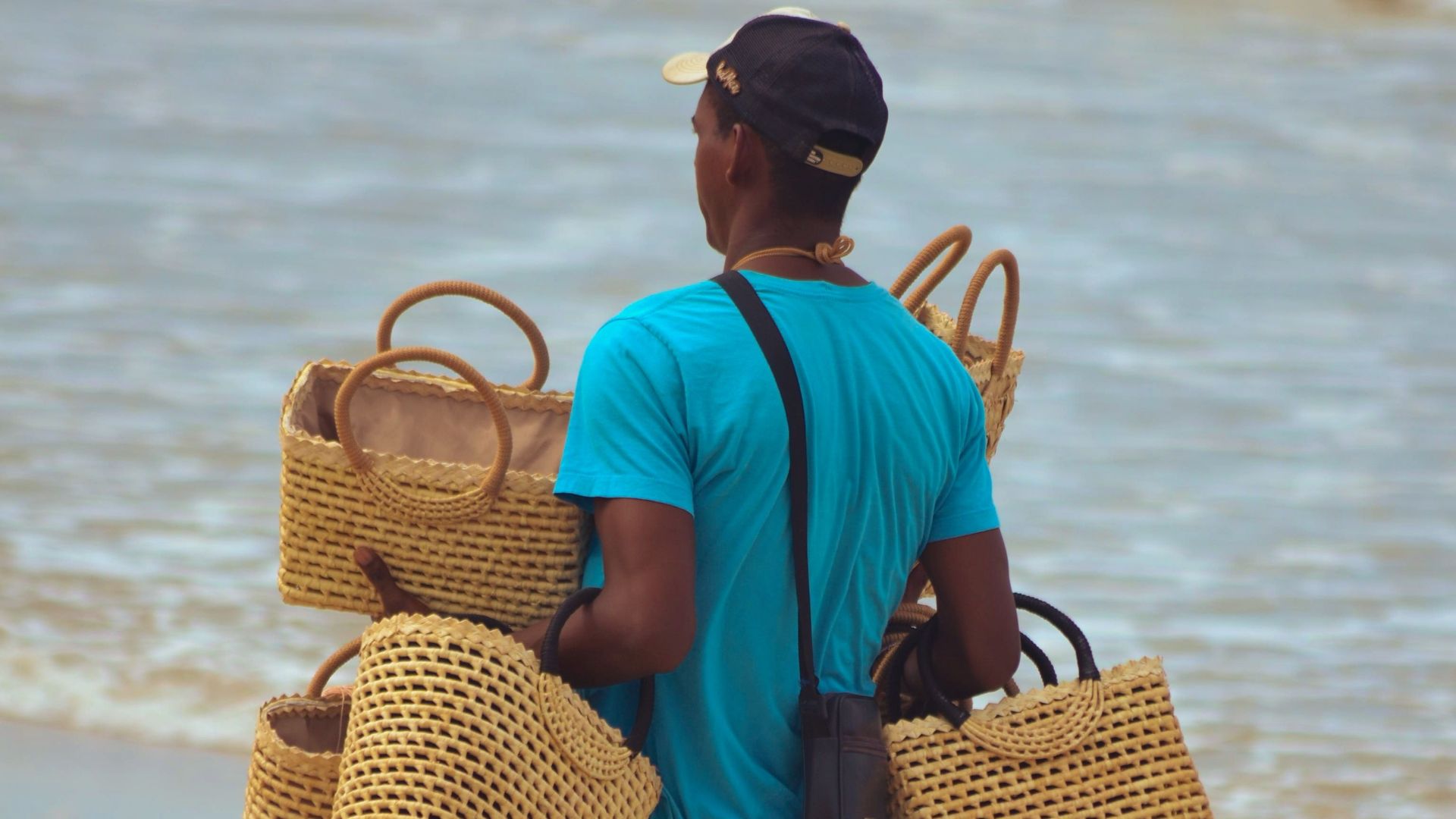 A vendor walking on a sandy beach carrying handmade baskets, showcasing local craftsmanship.