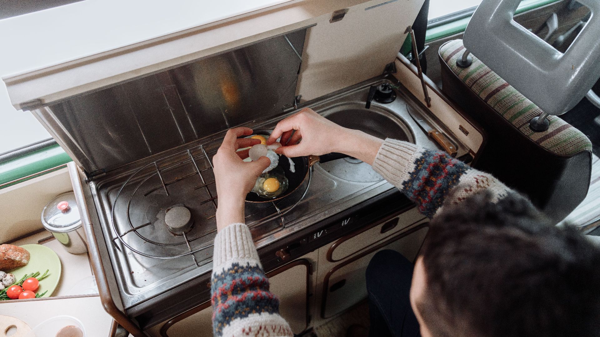 A person cracking eggs into a pan on a compact indoor stove setup. Cozy atmosphere.