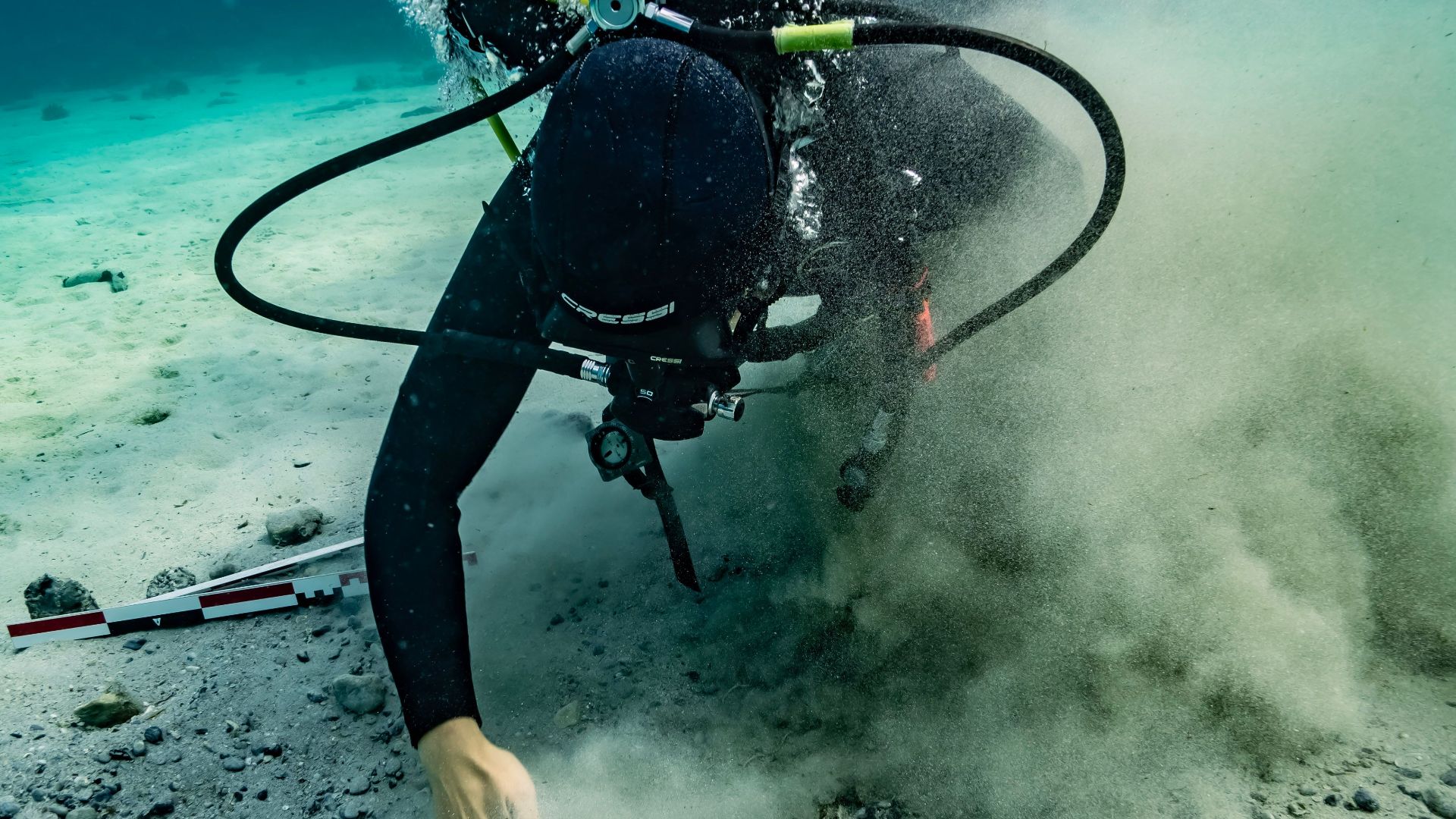 A scuba diver inspects the seabed underwater in Croatia, surrounded by bubbles and sand.