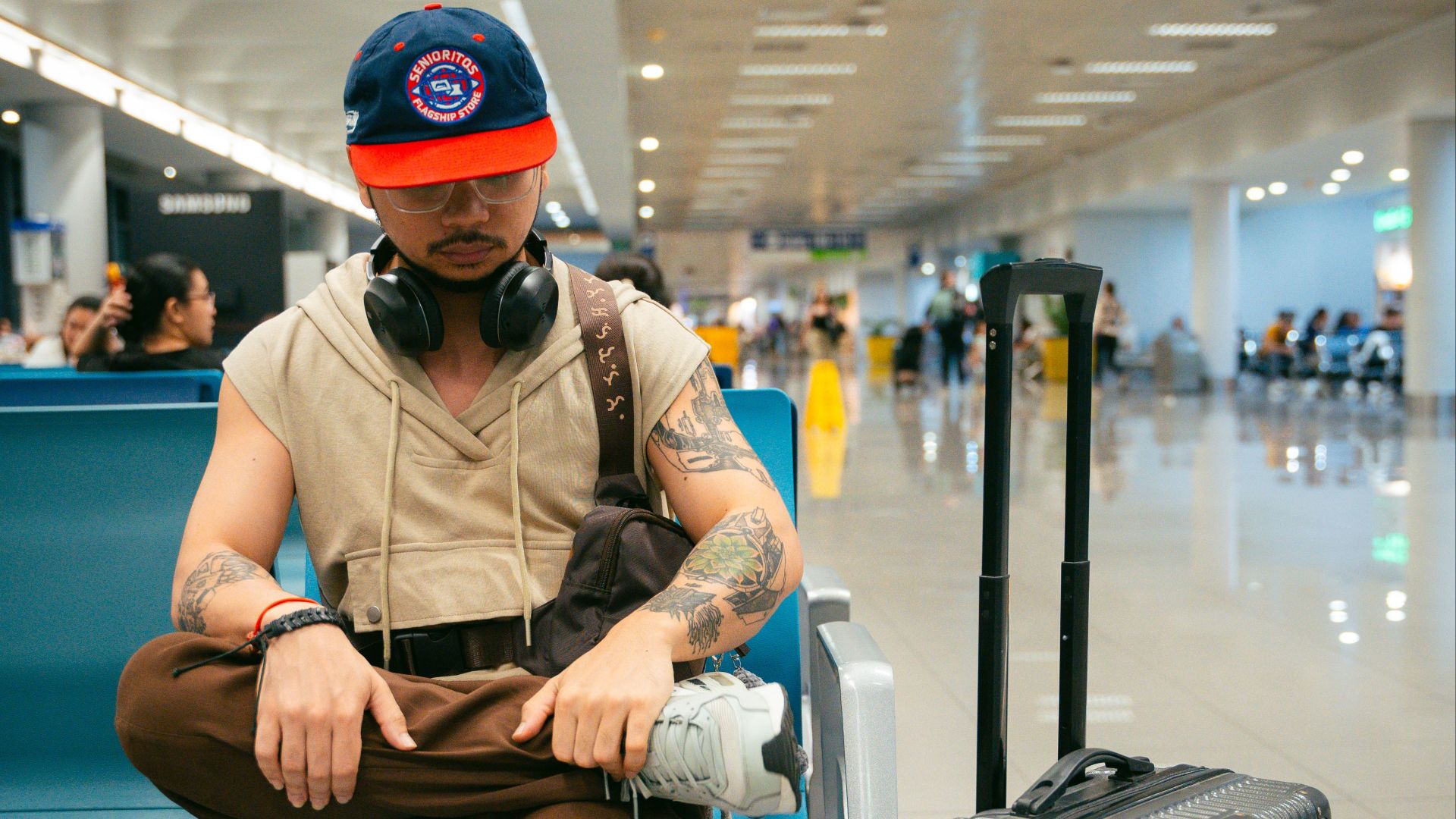 Stylish man in airport lounge with luggage, headphones, millennial fashion, ready for journey.