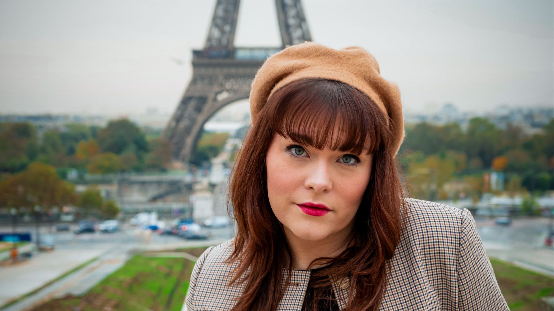 Chic woman in autumn attire poses gracefully in front of the Eiffel Tower.