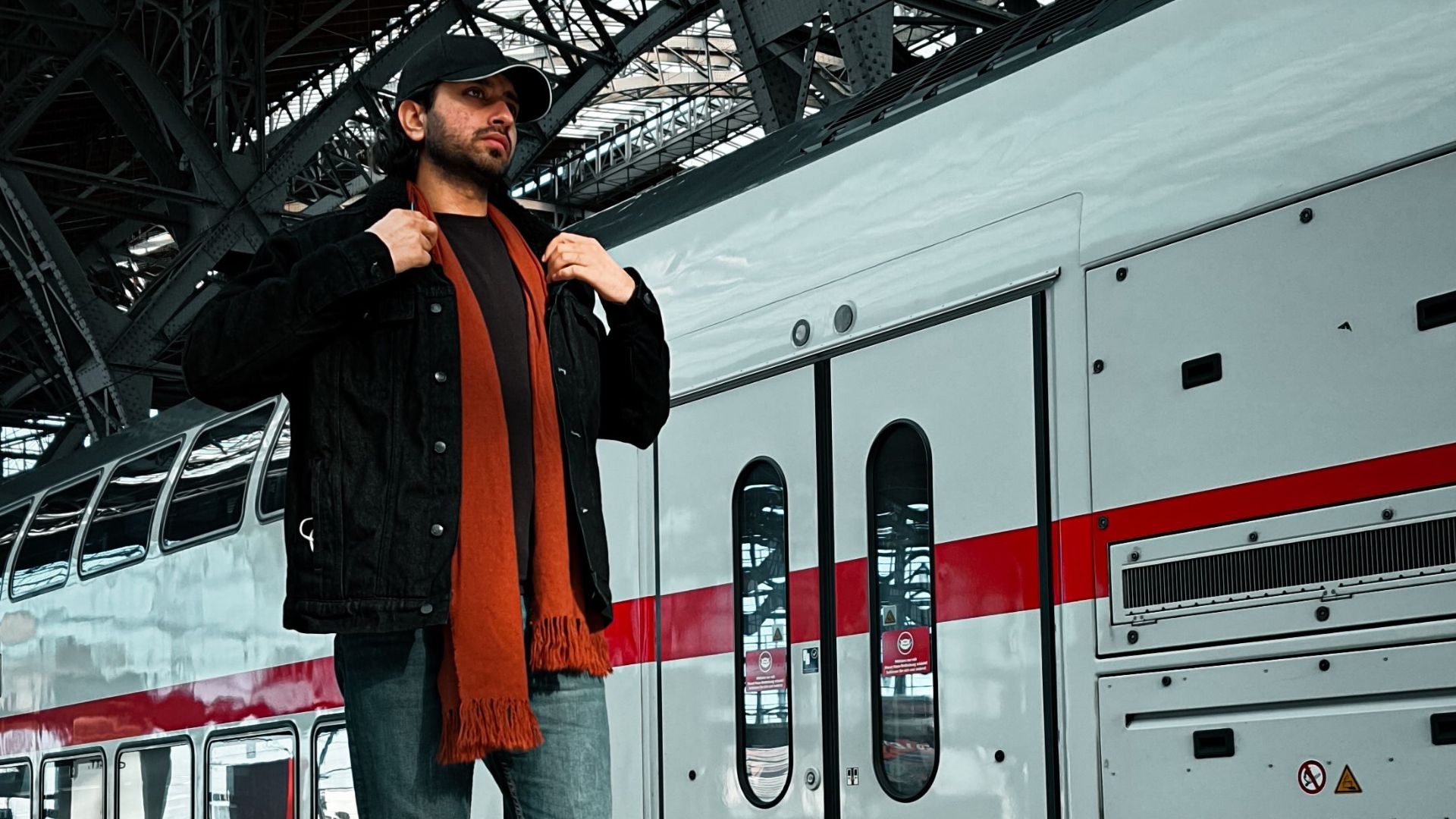 Casually dressed man standing on a platform at Leipzig Train Station with a train in the background.