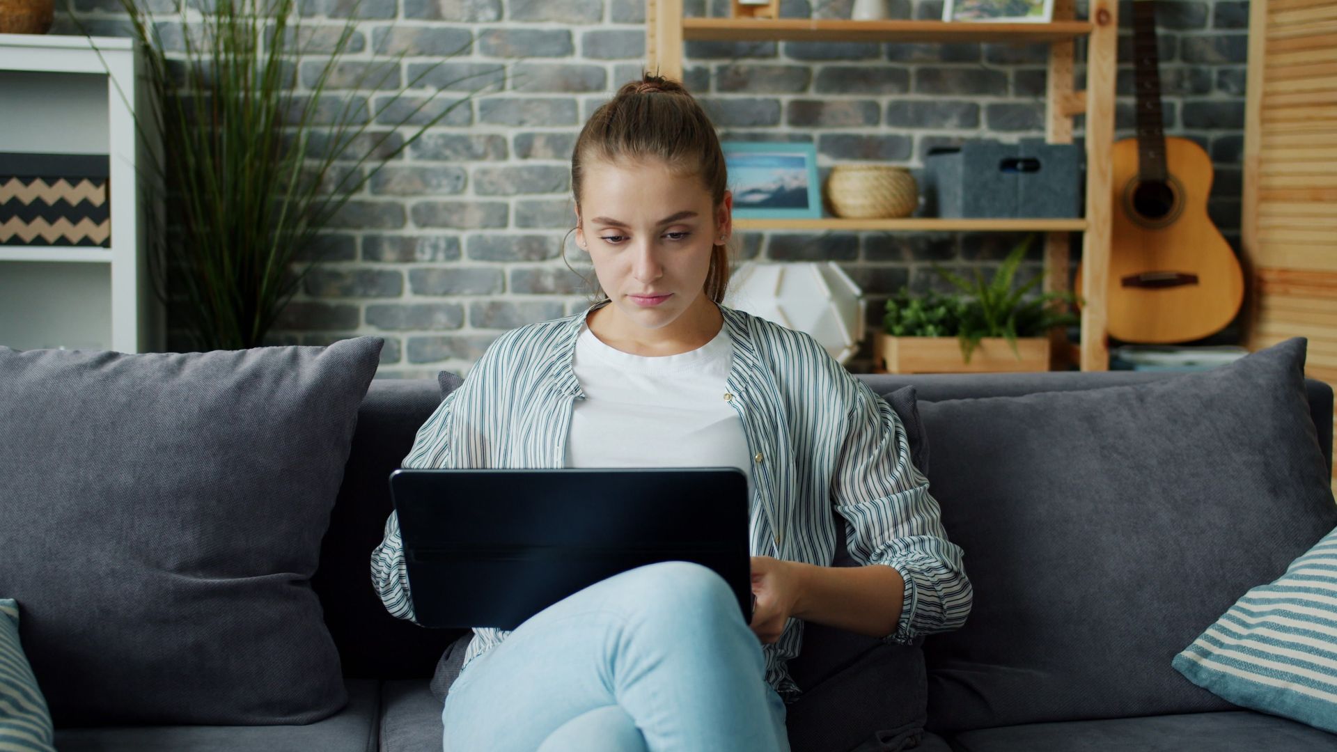 Young woman sitting on a sofa using a laptop in a home setting.