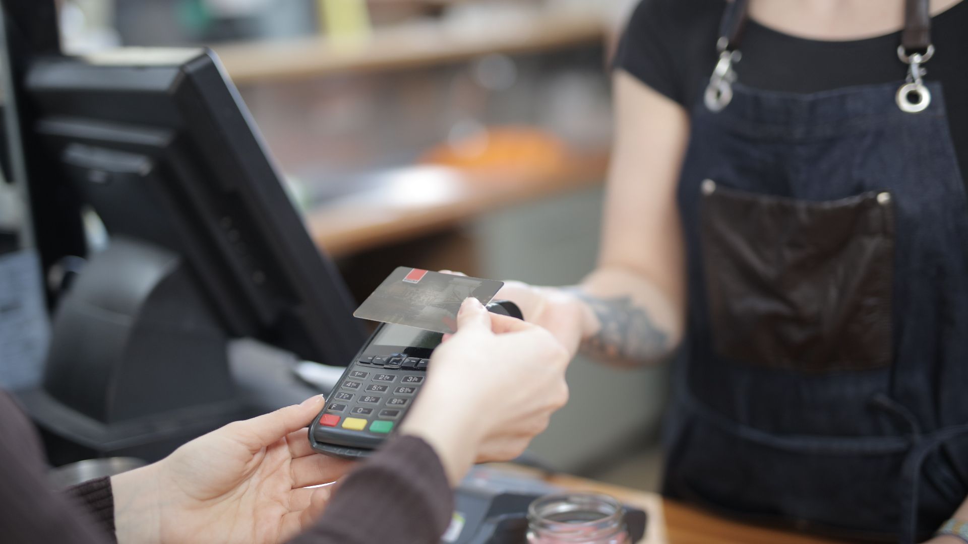 Close-up of customer and cashier during a credit card transaction at a store counter indoors.