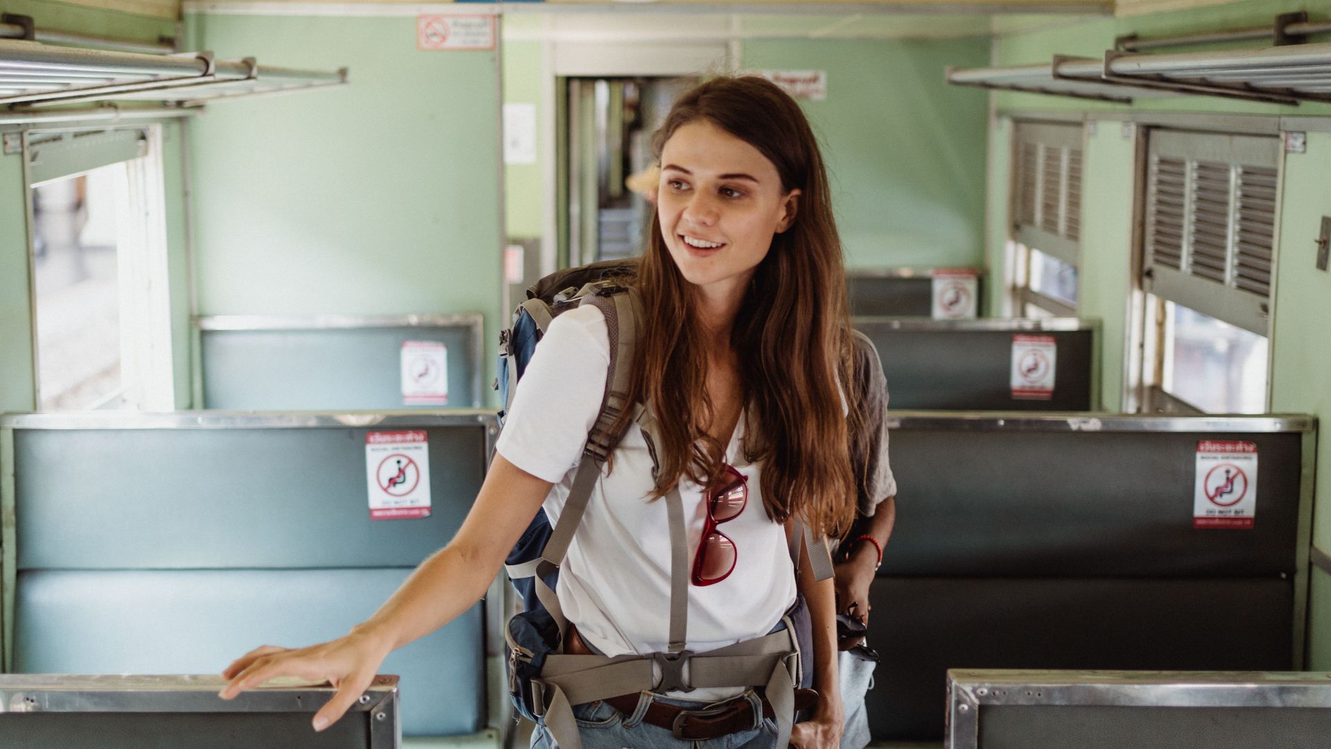 A young woman with a backpack walking inside an empty train cabin, symbolizing travel and adventure.