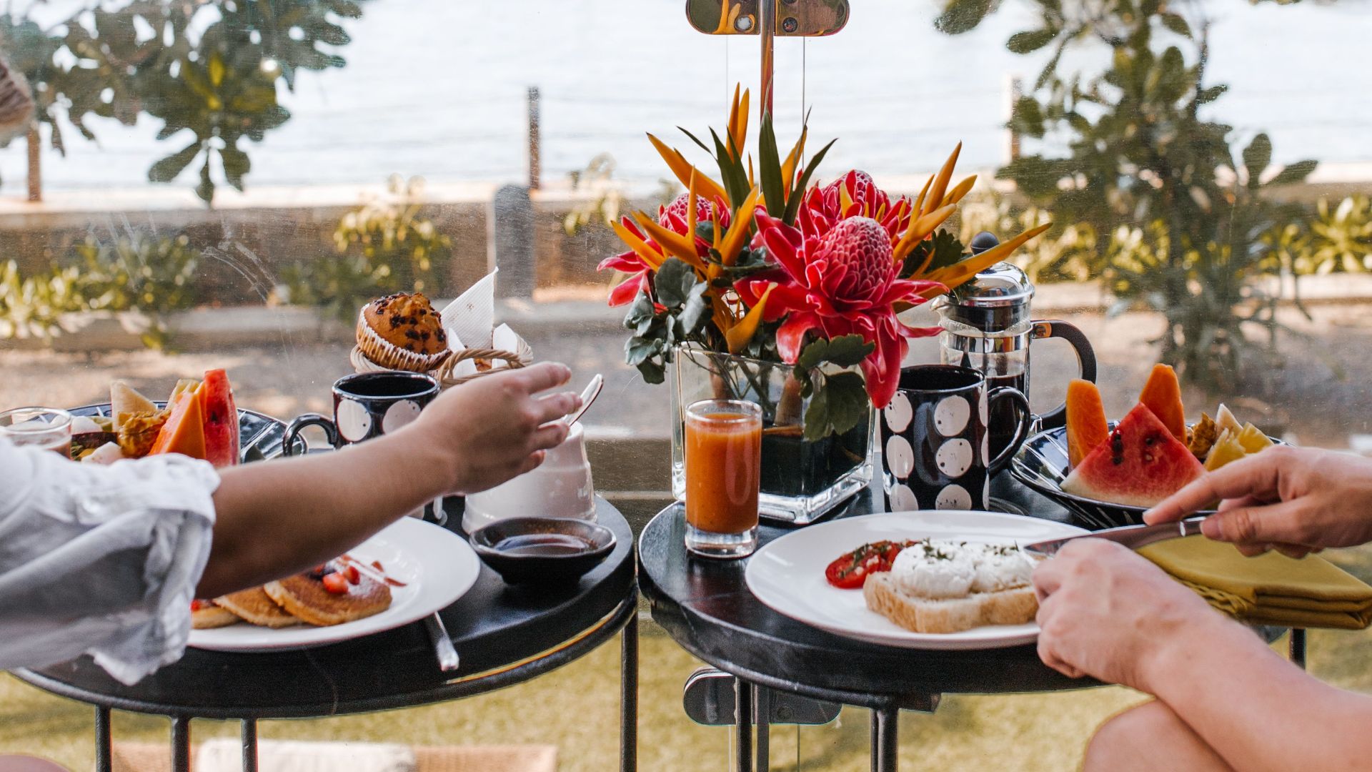 Crop anonymous man and woman sitting on terrace and having breakfast with picturesque sea view during summer holidays in tropical resort
