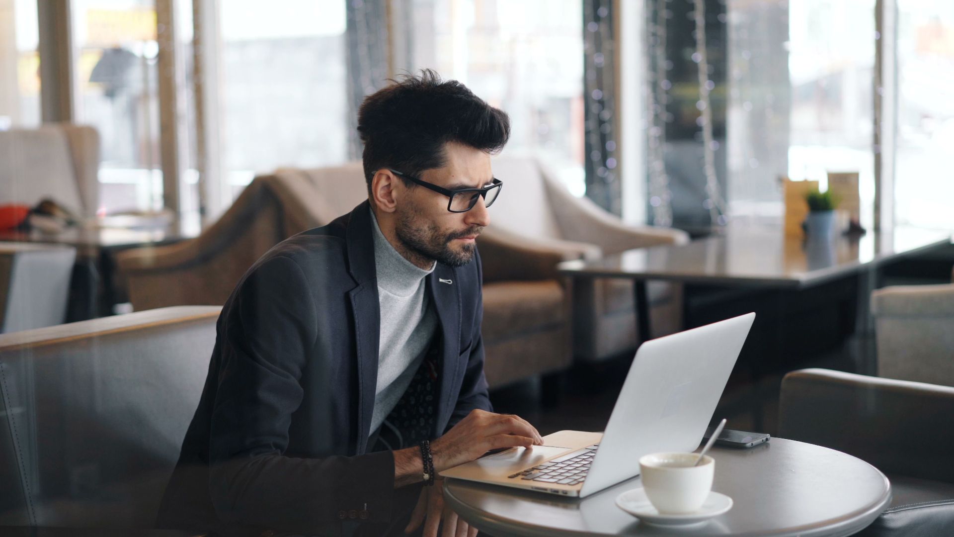 Focused businessman working on a laptop in a stylish cafe, drinking coffee.