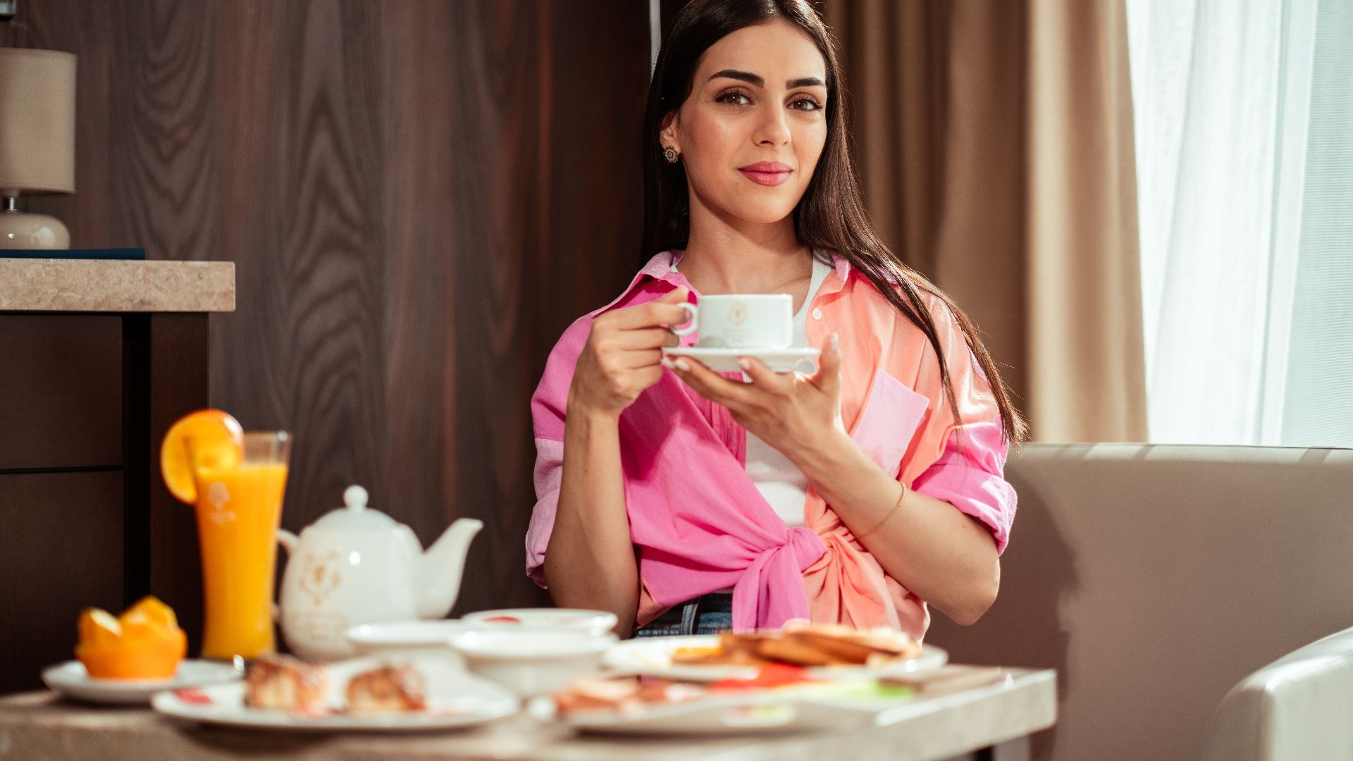 Woman enjoying a leisurely breakfast indoors with tea and juice in Baghdad hotel.