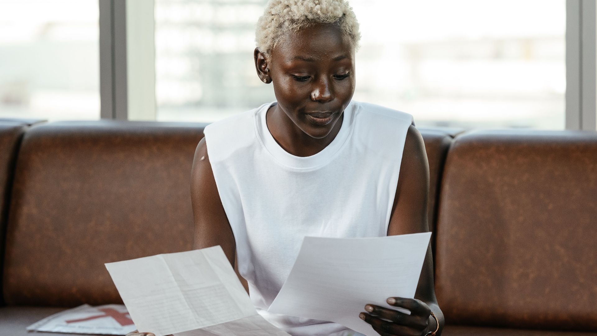 Concentrated African American female comparing important papers of report on leather sofa in office