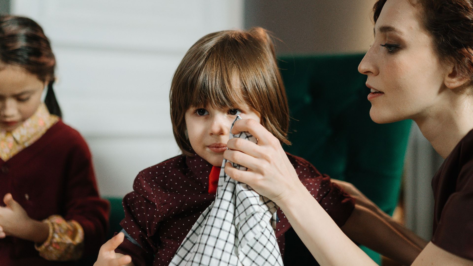 Woman assisting a child with a napkin during a meal indoors, highlighting care and family bonding.