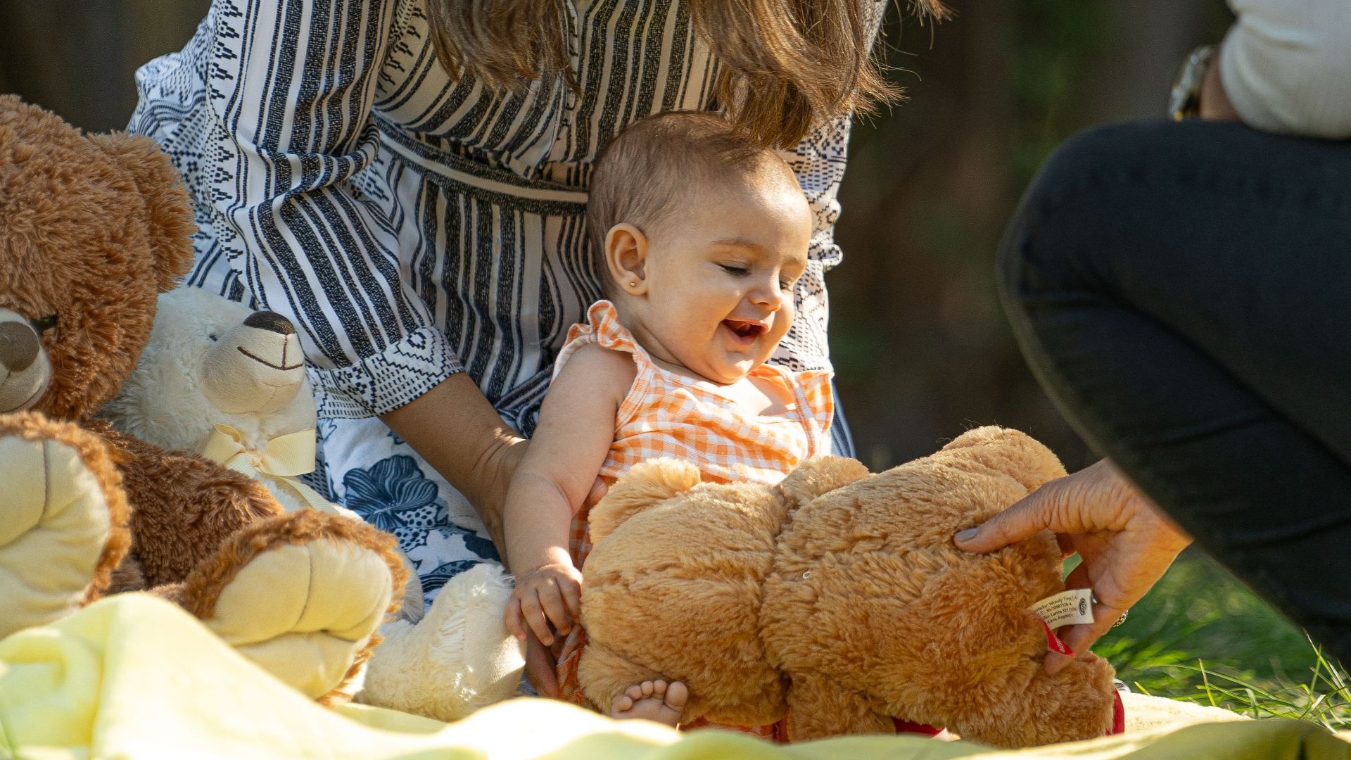 Adorable baby enjoying playtime with teddy bears outdoors on a sunny day.
