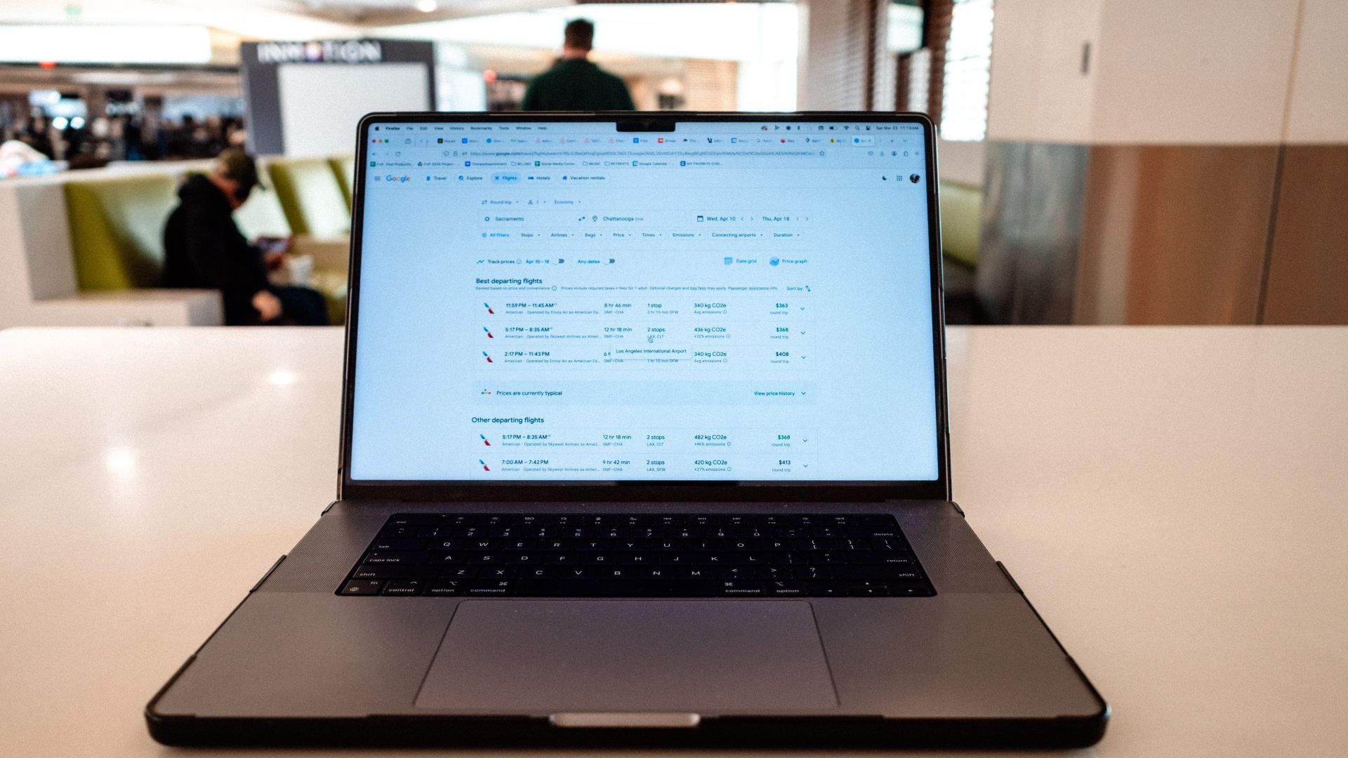 A modern laptop displaying flight schedules on a white table in an airport lounge.