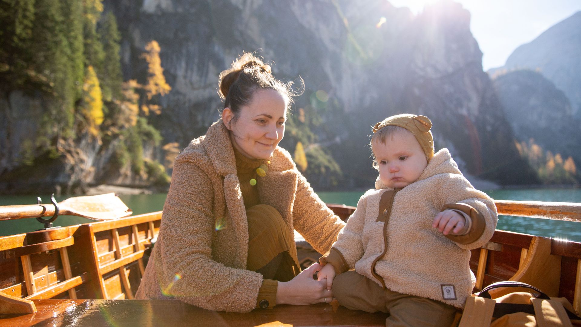 A mother and child enjoy a serene boat ride surrounded by mountains and nature, reflecting love and tranquility.