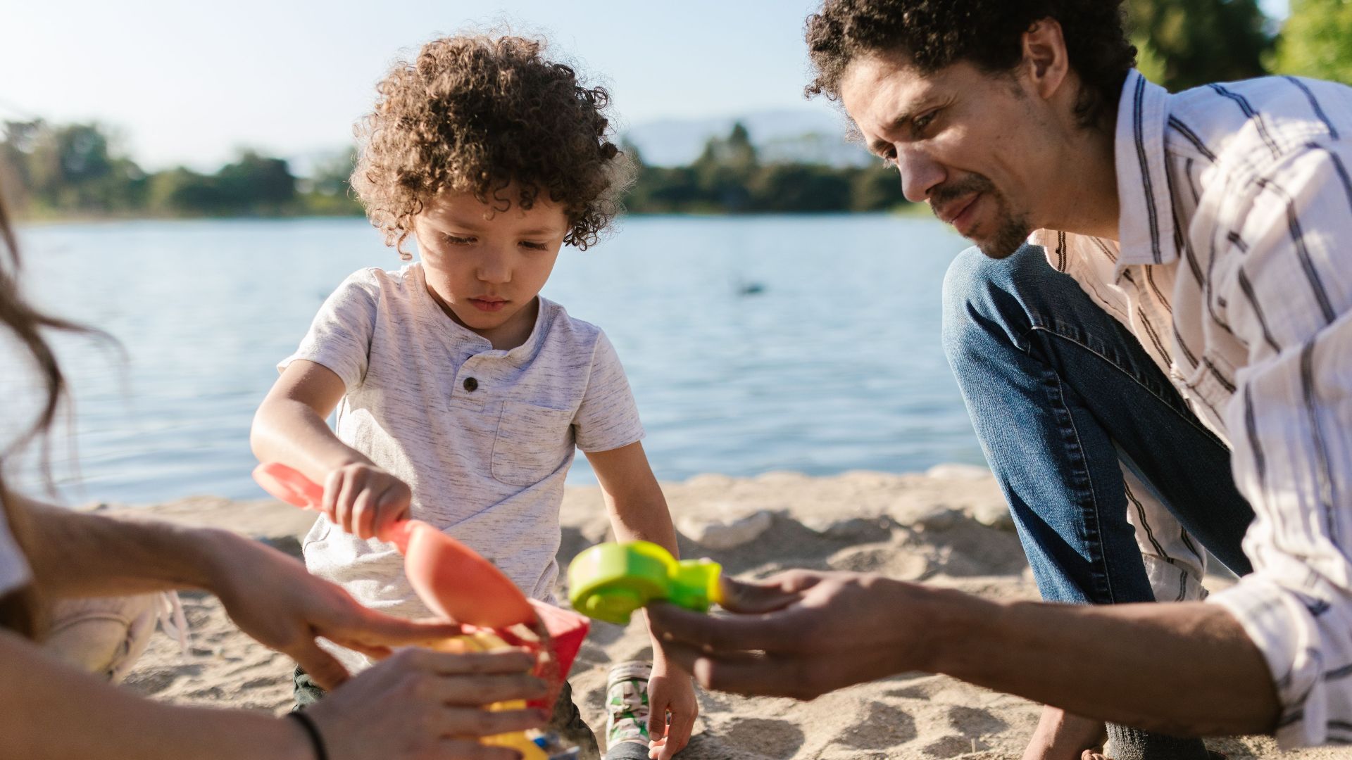 Father and son enjoying playtime with sand toys at the beach on a sunny day.