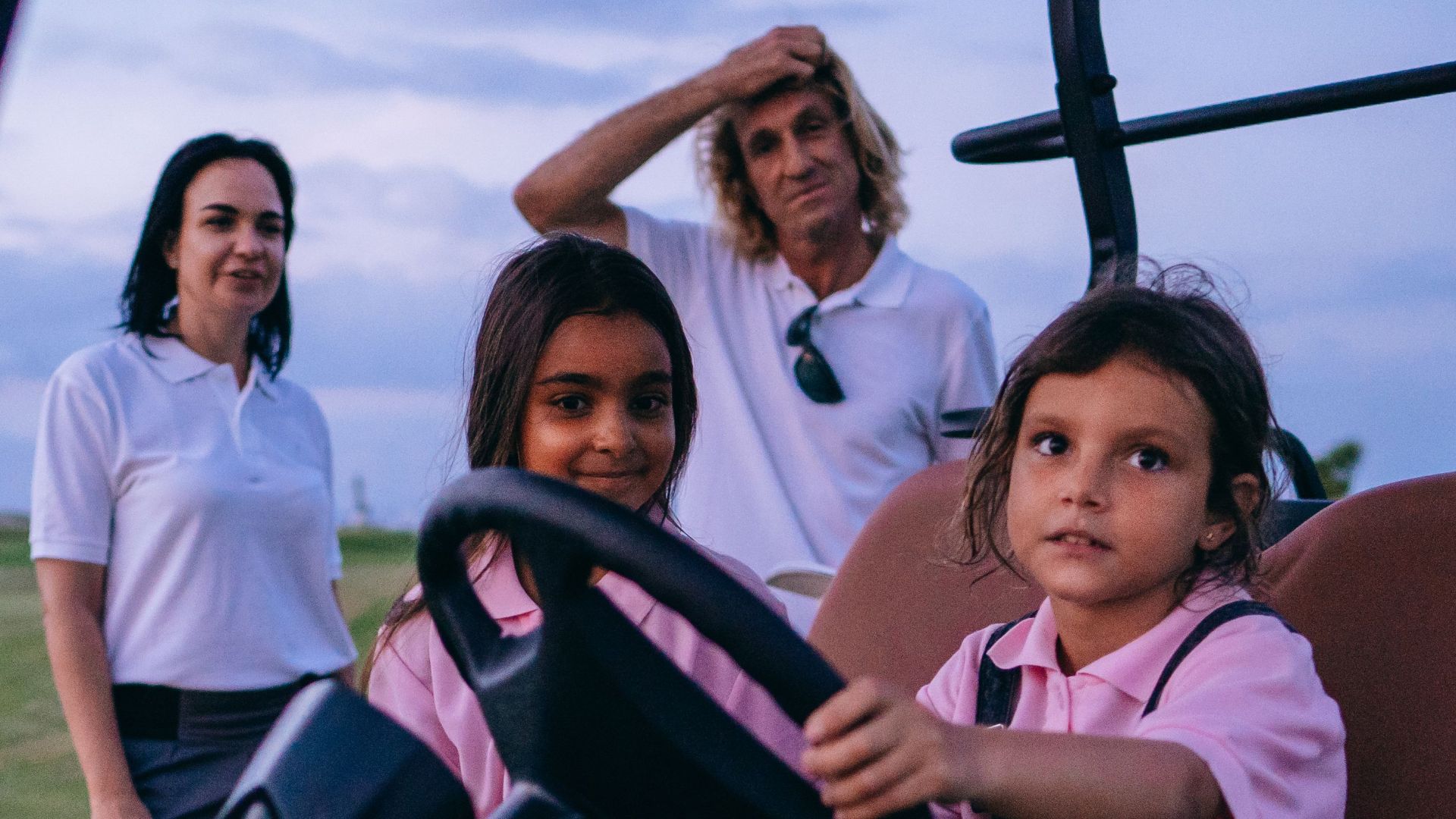 Family with kids having fun on a golf cart at a golf course during daylight.