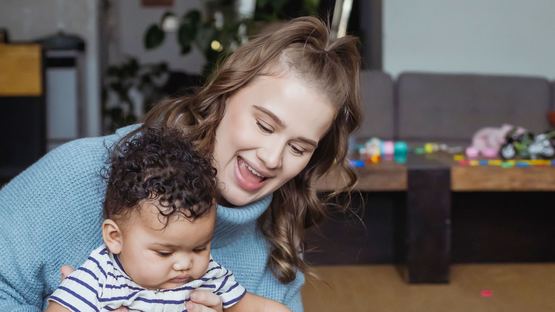 Woman playing with ethnic children on blanket on floor in light room near couch and table