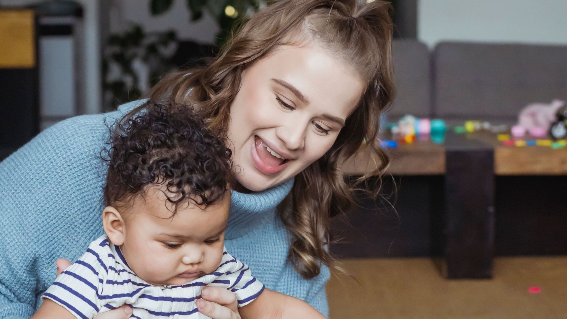 Woman playing with ethnic children on blanket on floor in light room near couch and table
