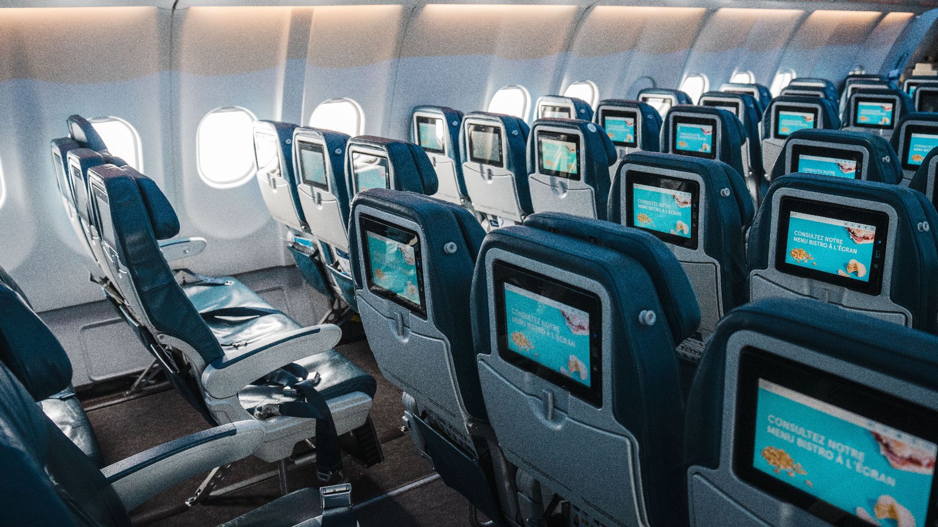 Empty airplane interior highlighting rows of seats with touchscreens, offering a modern in-flight experience.
