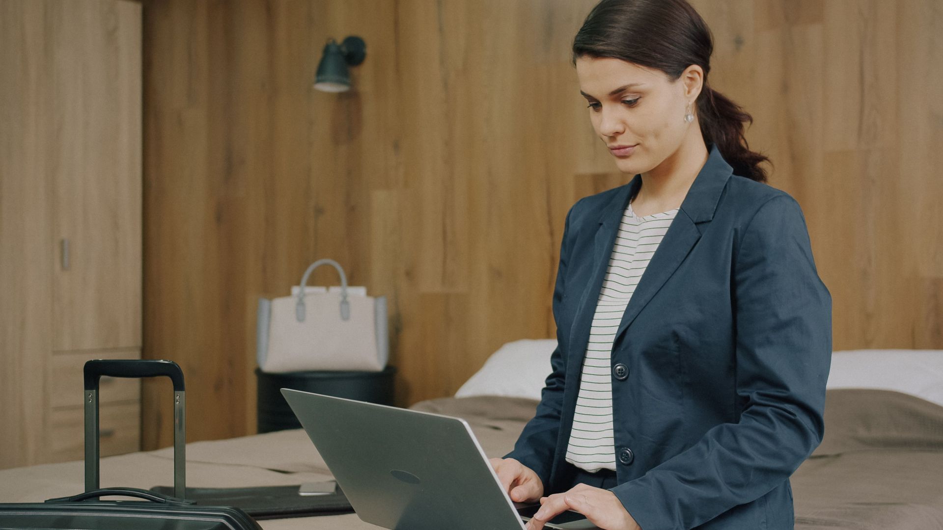 Professional woman using a laptop in a hotel room, preparing for business travel.