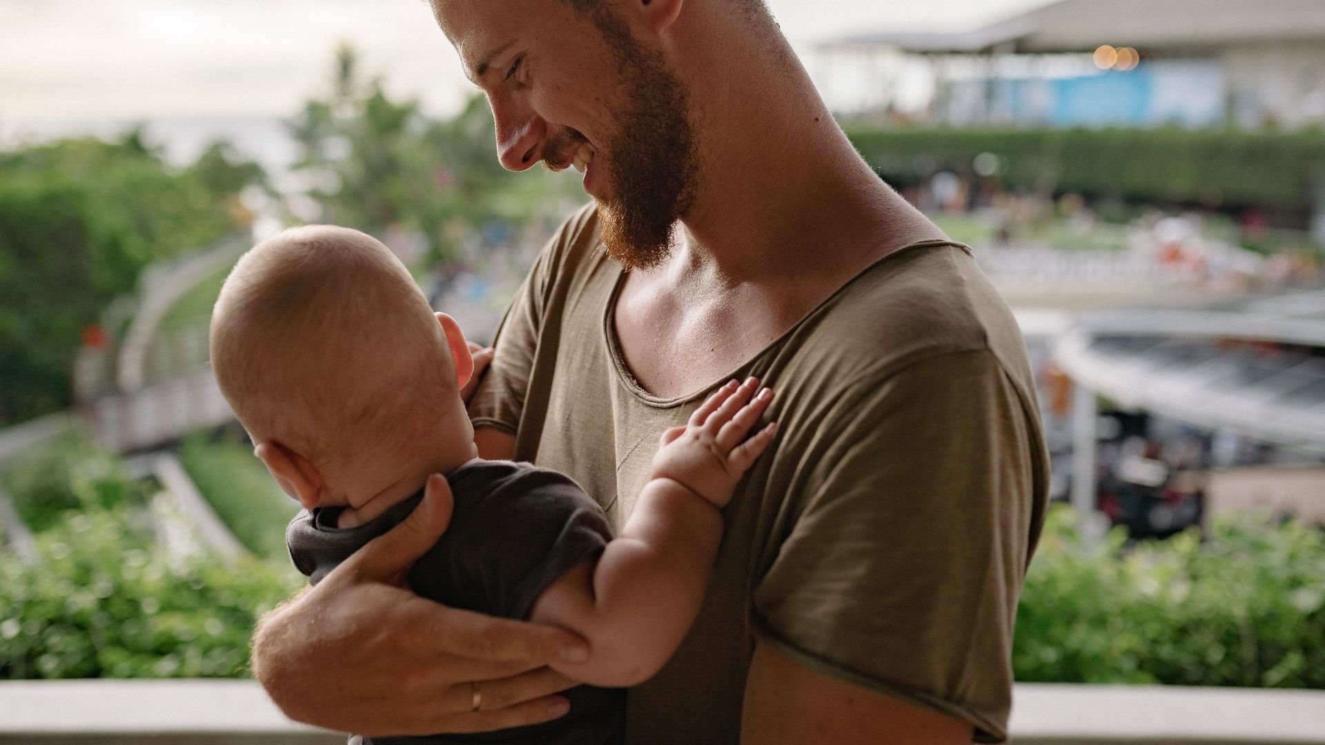 A bearded father holds his baby, sharing a tender moment outdoors.