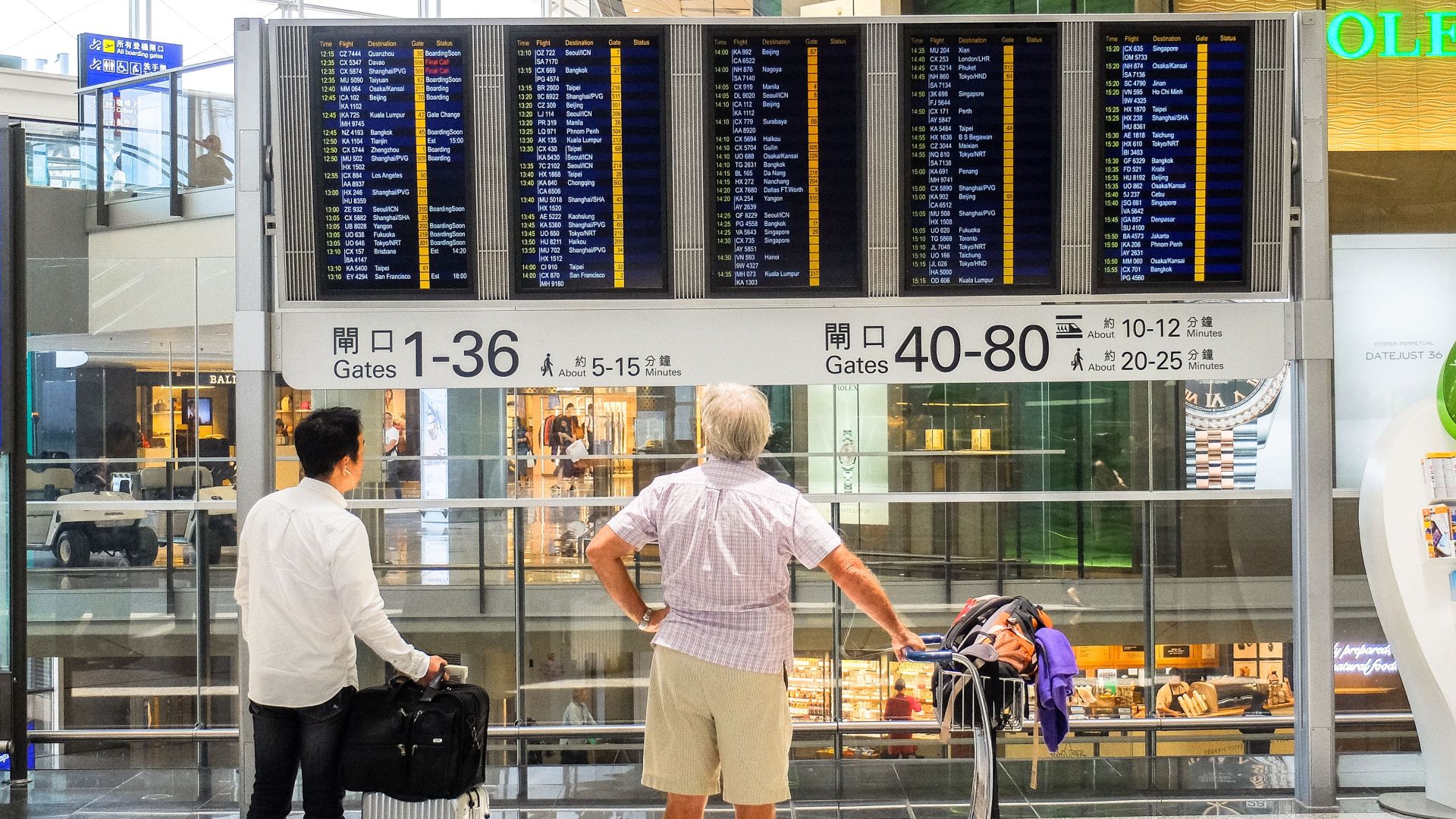 Passengers review flight information on a digital board in Hong Kong airport terminal.