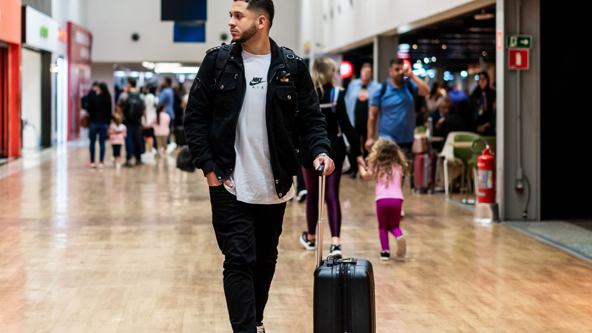 Man walking with luggage in a crowded airport terminal, heading to boarding gates.