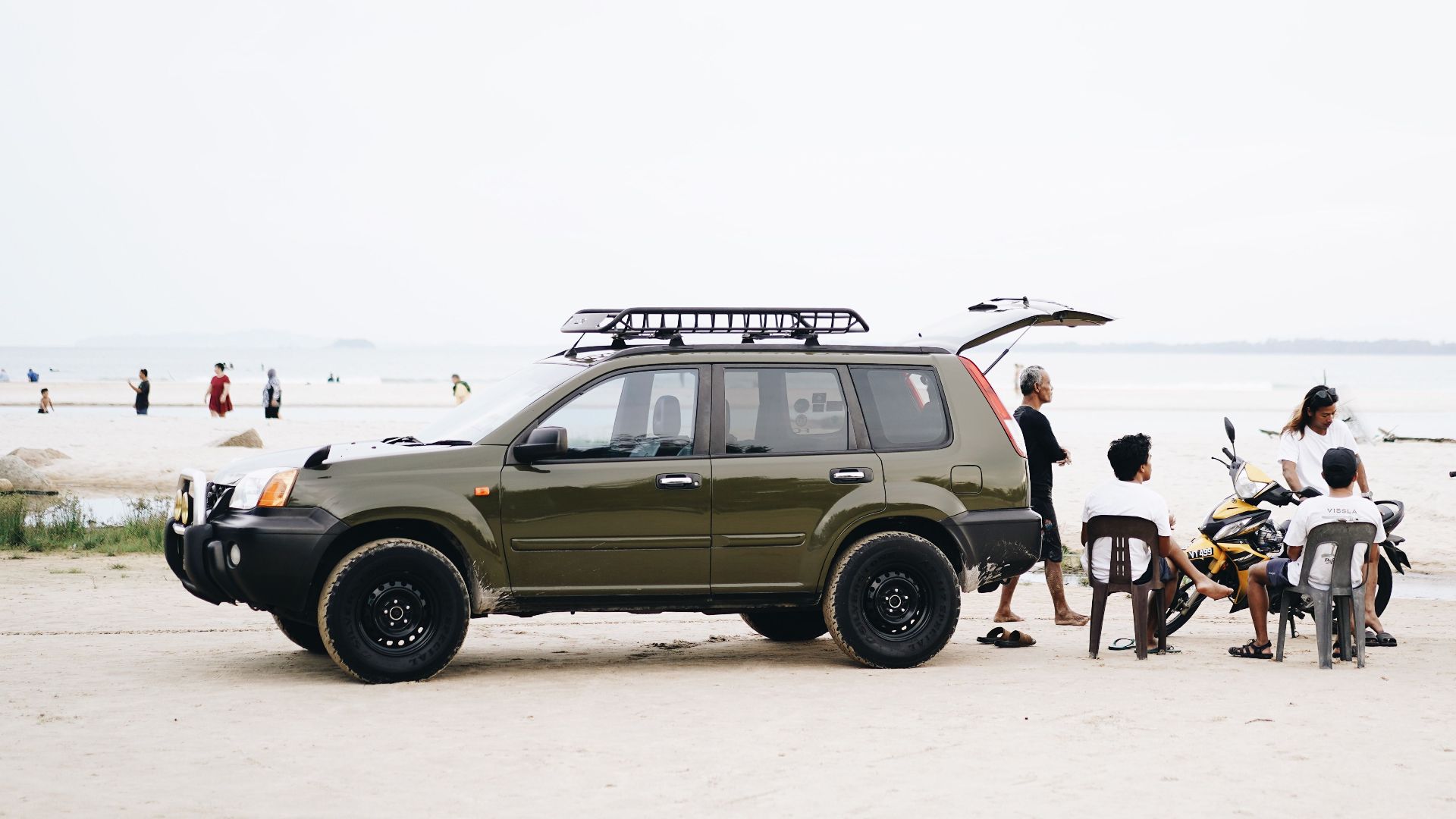 Group of people relaxing on the beach with an SUV and motorbike.