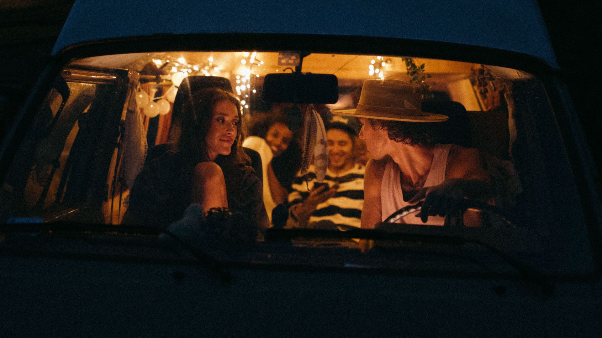 Four friends enjoying a night road trip in a cozy van with warm interior lights.
