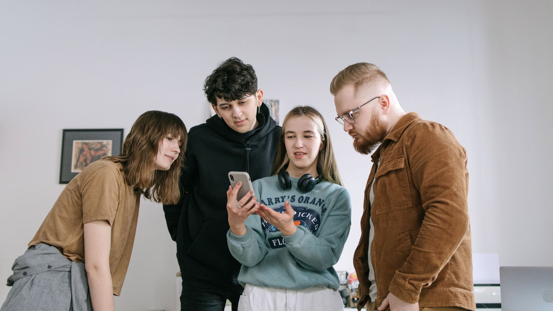 Group of young adults reviewing content on a smartphone in an office setting.