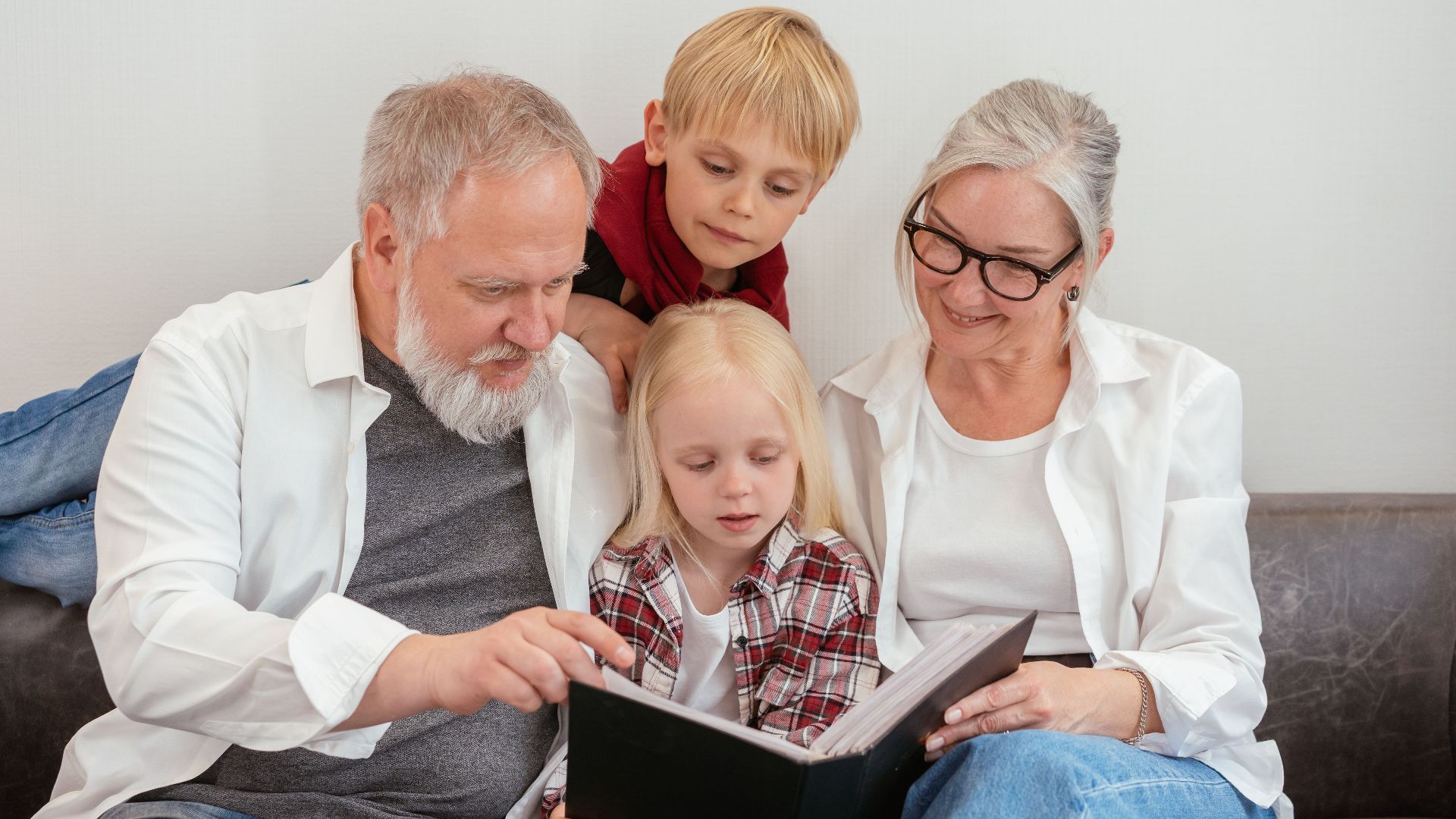 Grandparents and grandchildren reading a photo album on the couch, embracing family bonds and love.