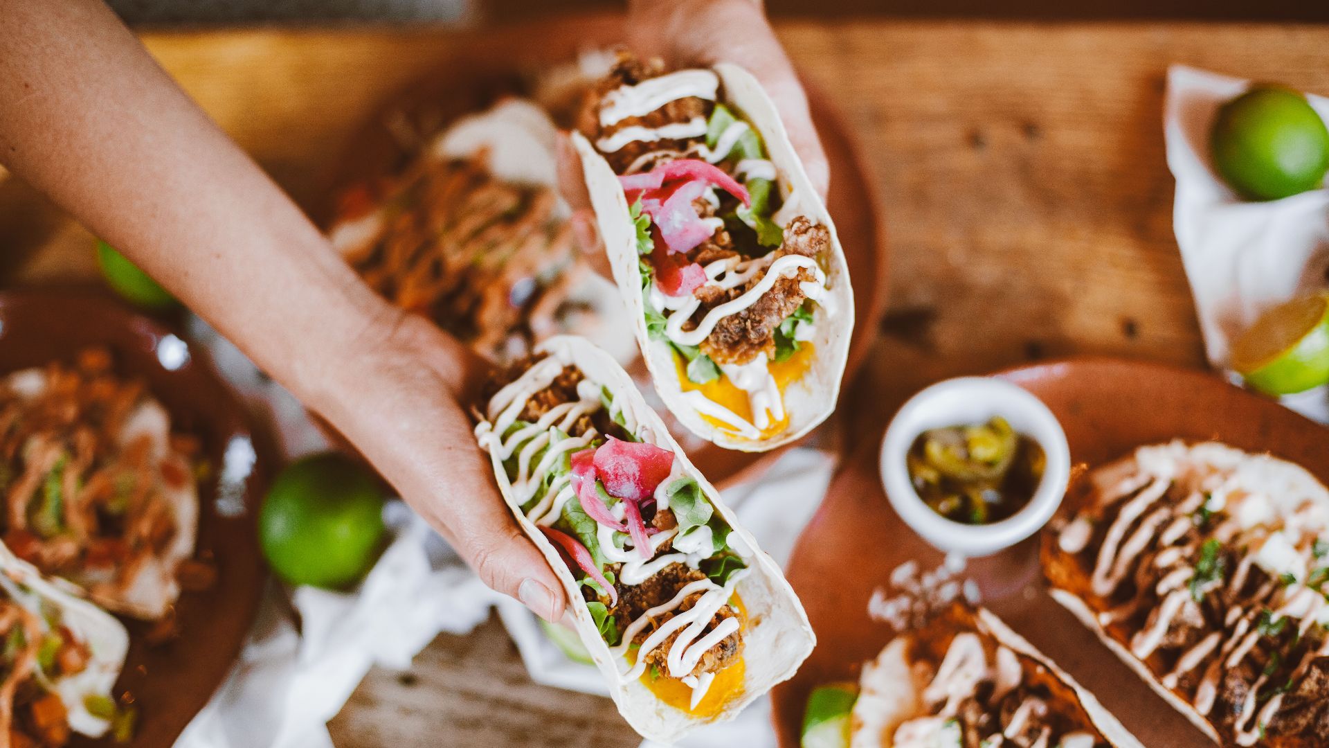 Delicious handheld tacos with fresh toppings and lime on a wooden table.
