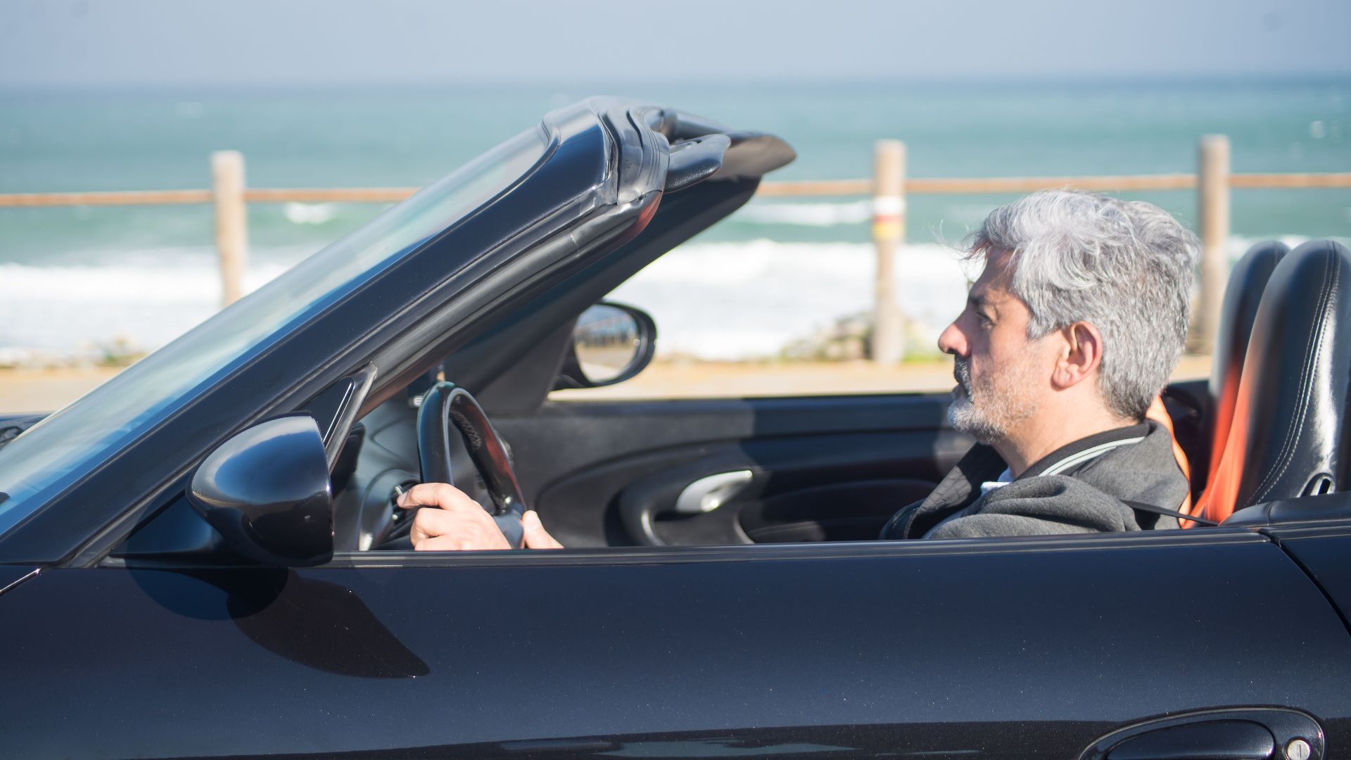 Senior man with gray hair drives a convertible along the scenic Portuguese coast.