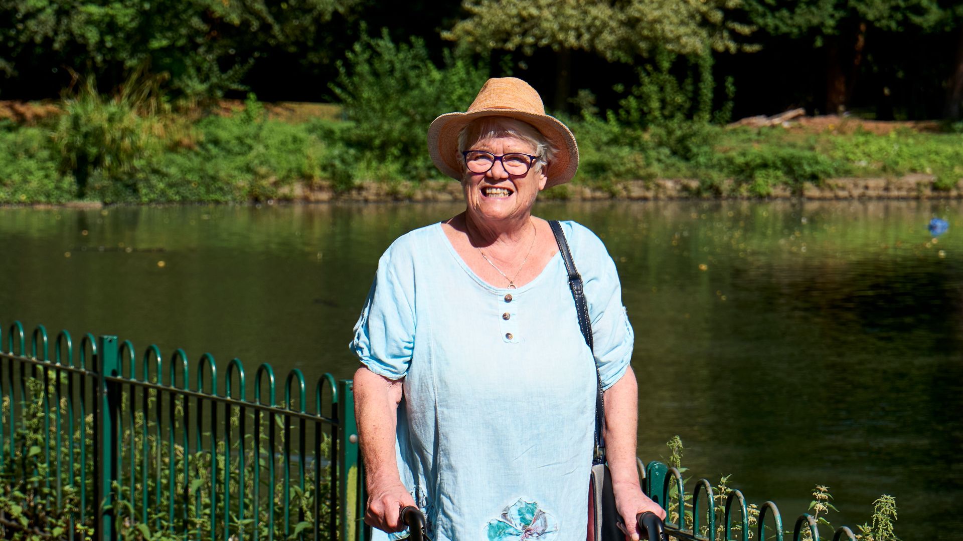 Senior woman with walking frame enjoying a sunny day by the pond.