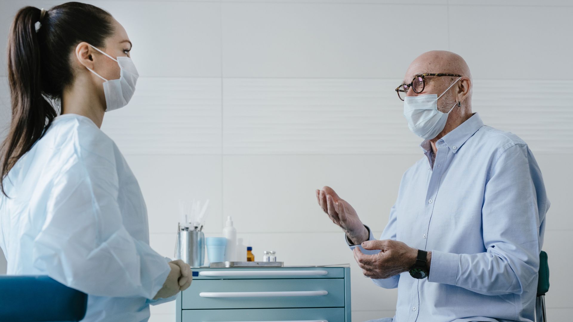 A senior adult patient discusses health concerns with a masked medical professional in a clinic setting.