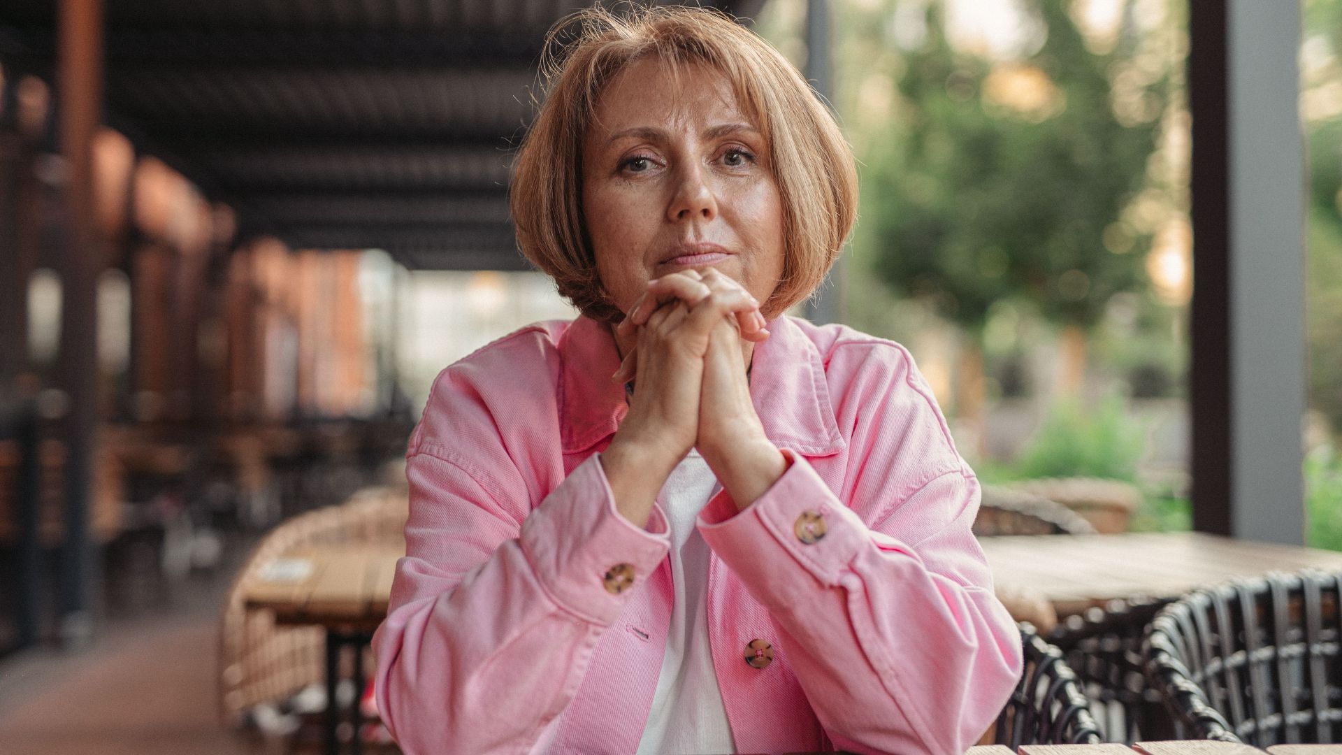 Portrait of a senior woman in pink, sitting outdoors in a contemplative pose.
